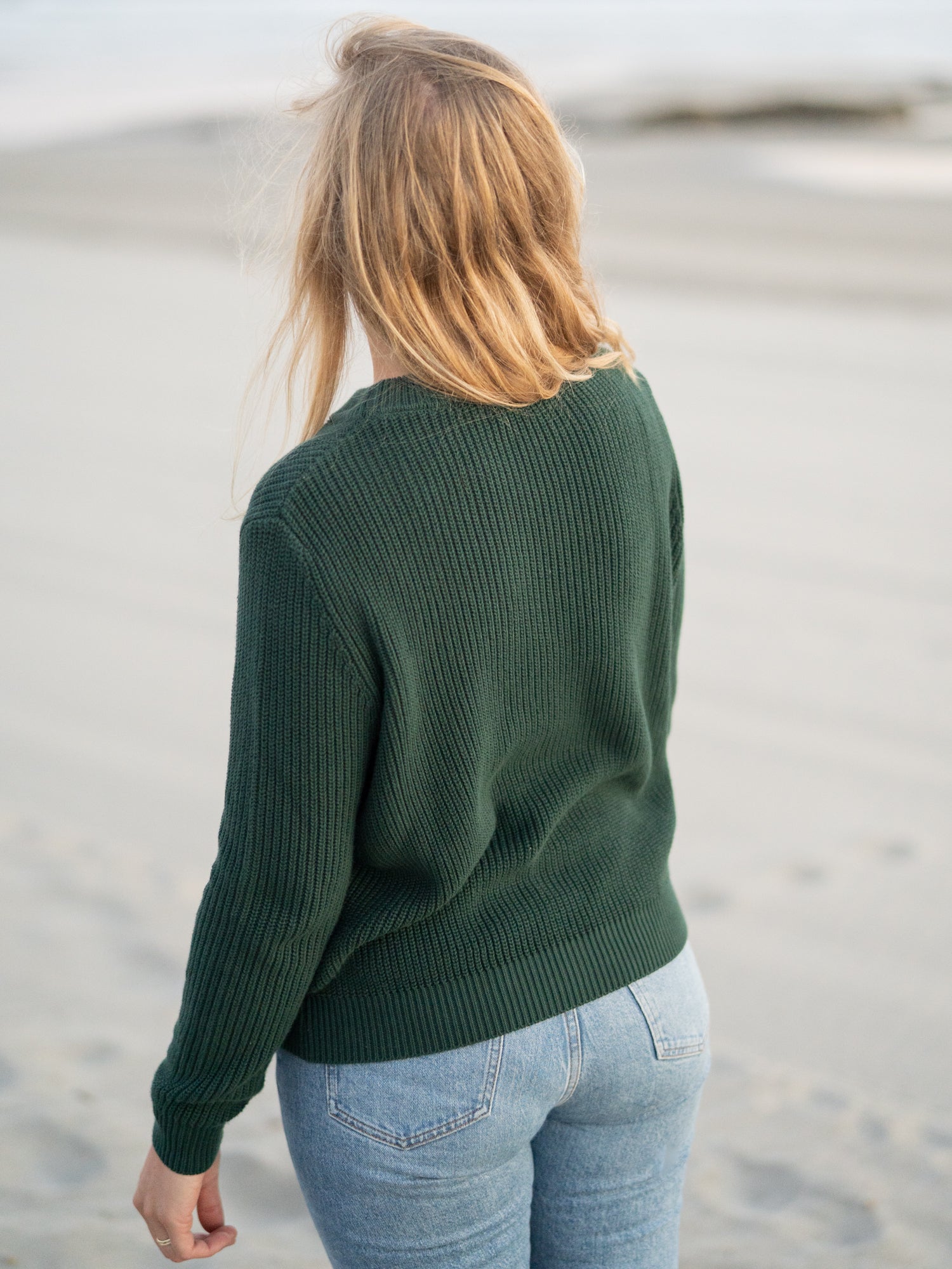 Isi trägt unseren FUXBAU 4Seasons STrickpullover in waldgrün aus 100% GOTS zertifizierter Biobaumwolle am Strand in Portugal.