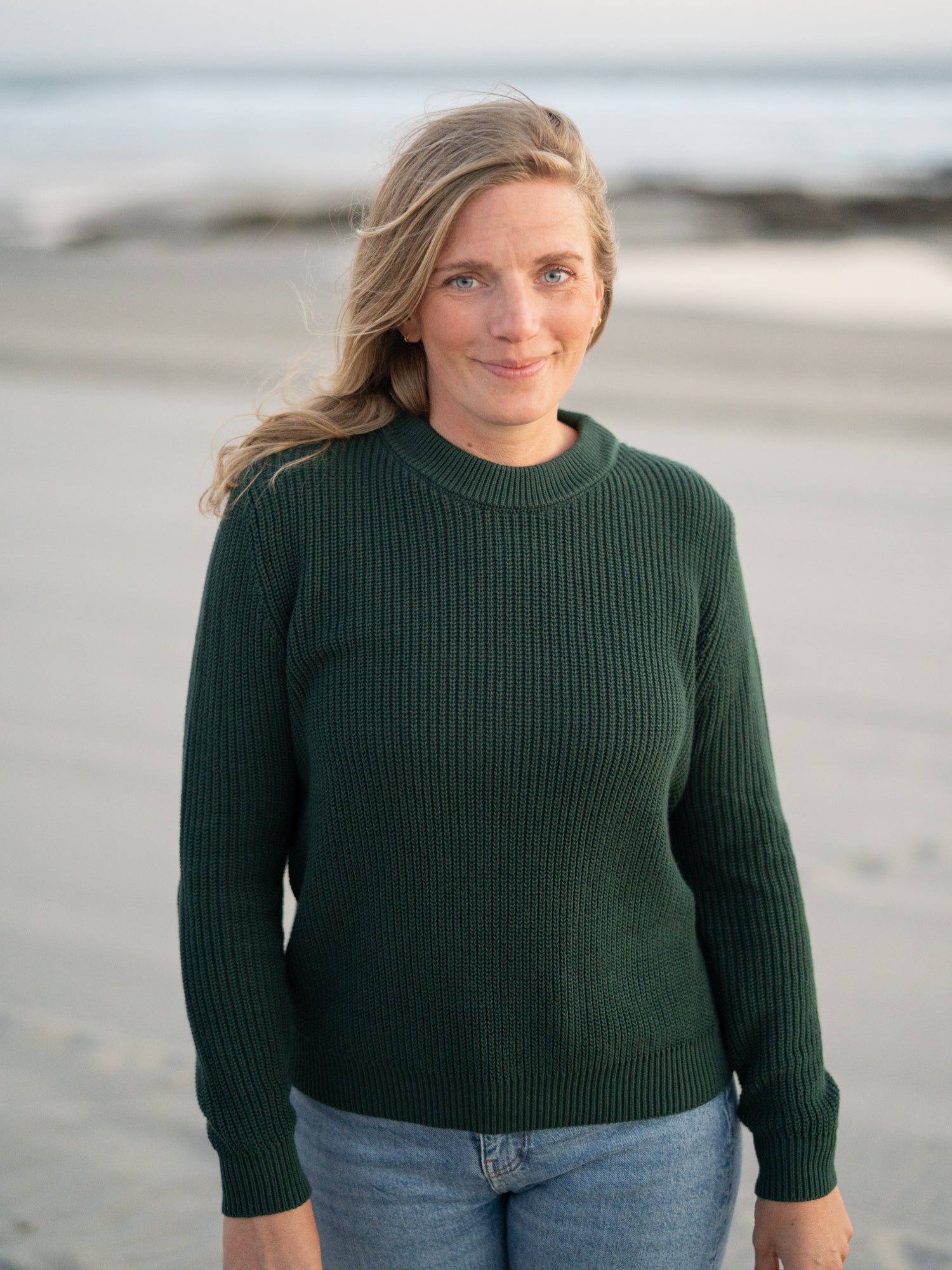 Isi trägt unseren FUXBAU 4Seasons STrickpullover in waldgrün aus 100% GOTS zertifizierter Biobaumwolle am Strand in Portugal.