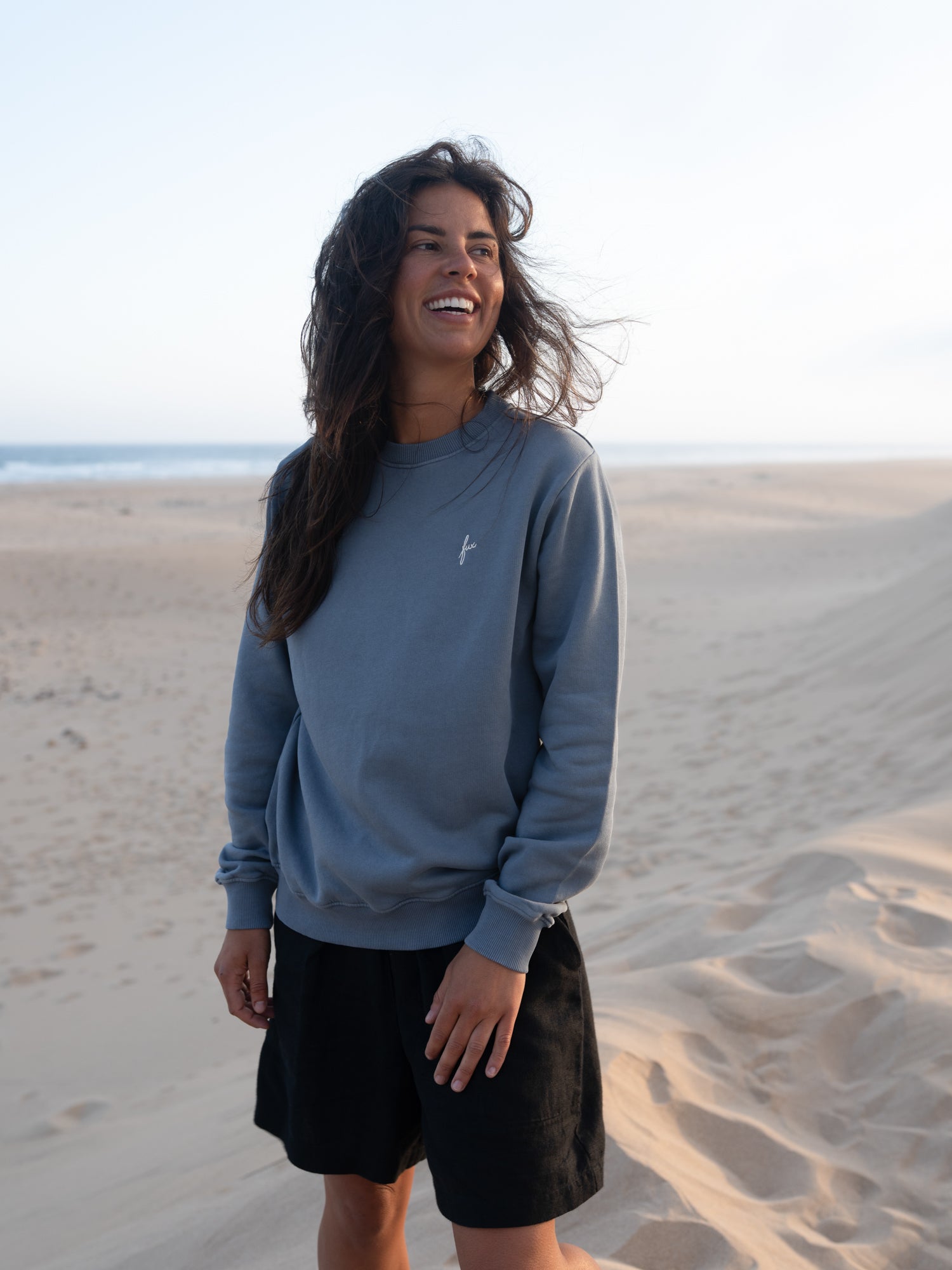 Nachhaltiger Frauen Pullover in Seeblau von FUXBAU vor heller Dünenlandschaft