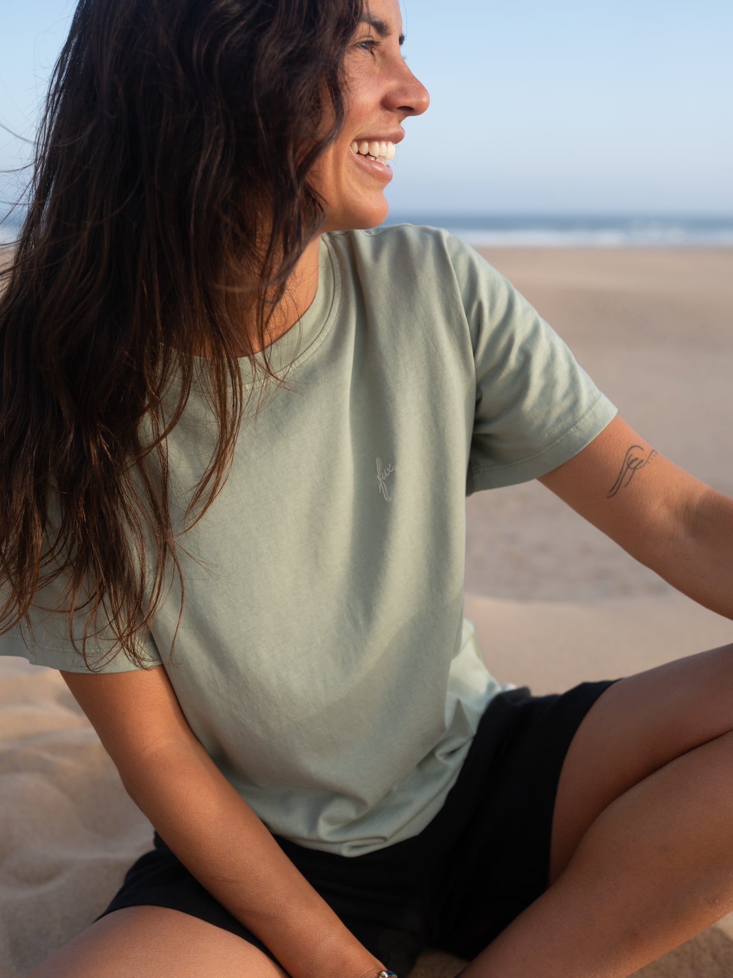 Frau trägt seegrünes FUXBAU T-Shirt aus Biobaumwolle am Strand in Portugal