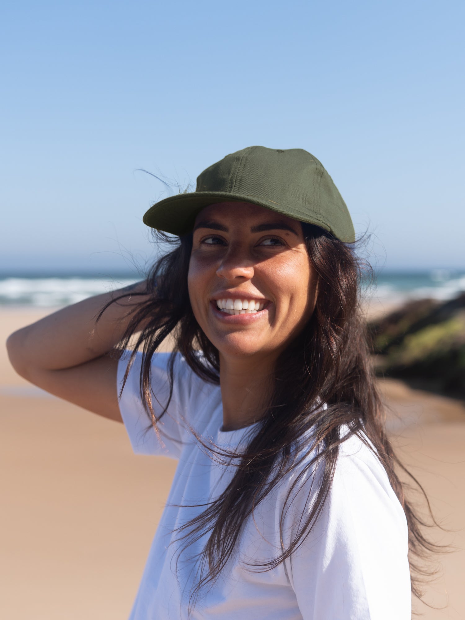 Frau trägt nachhaltige olivgrüne Dad Cap aus Biobaumwolle am Strand