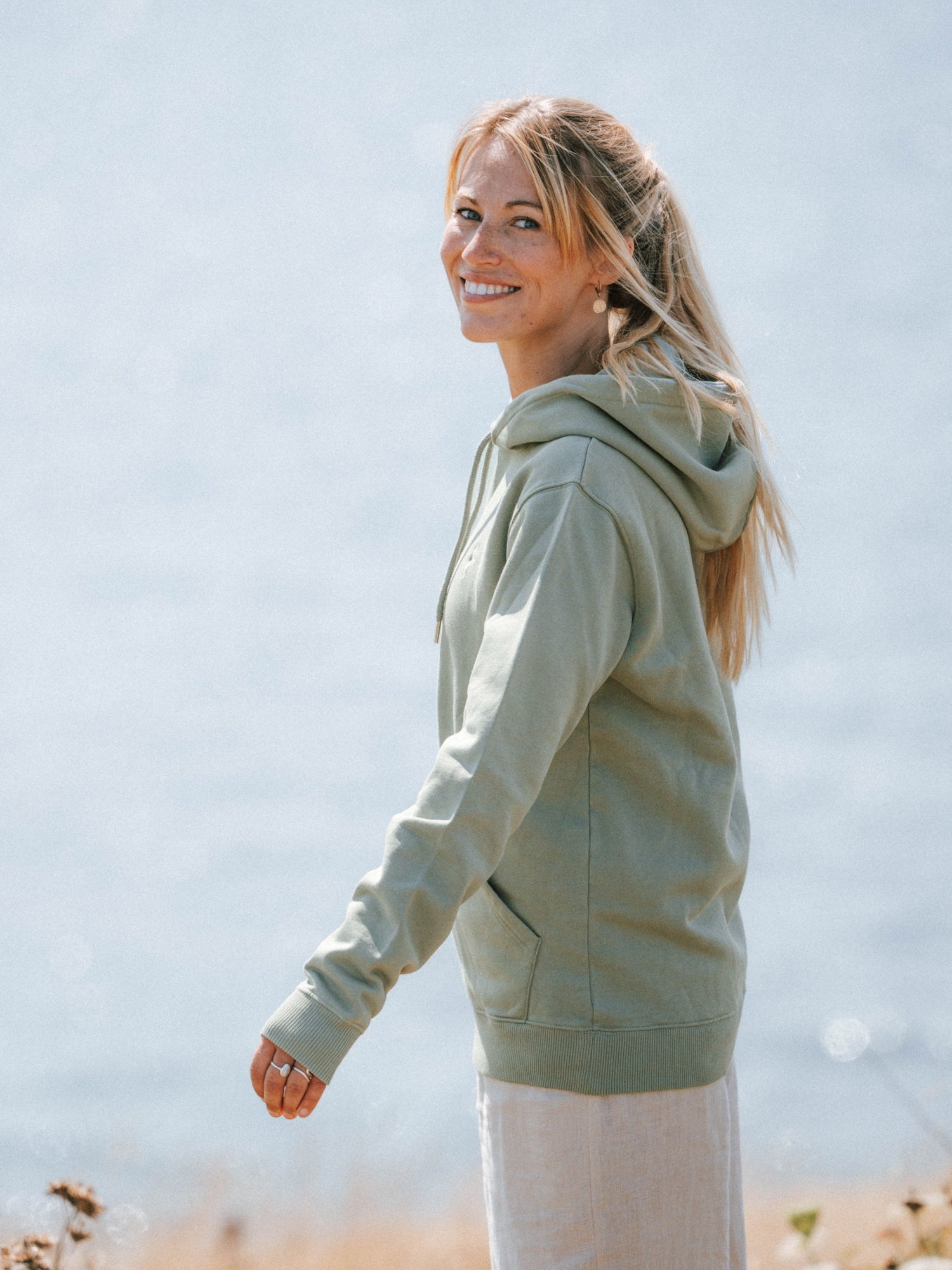 Unisex Hoodie in Seegras aus Biobaumwolle in seitlicher Ansicht am Meer