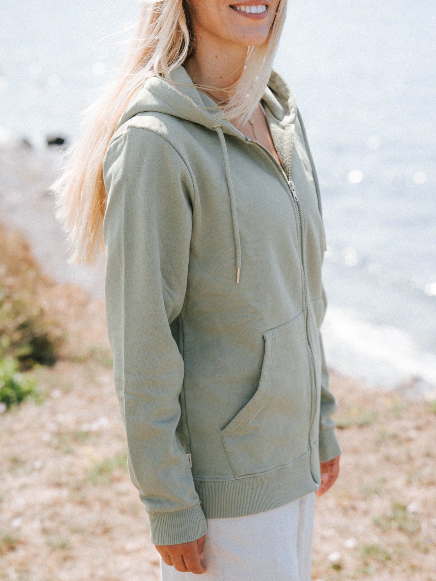 Unisex Sweatjacke in Seegras aus Biobaumwolle mit Kapuze und Reißverschluss am Meer