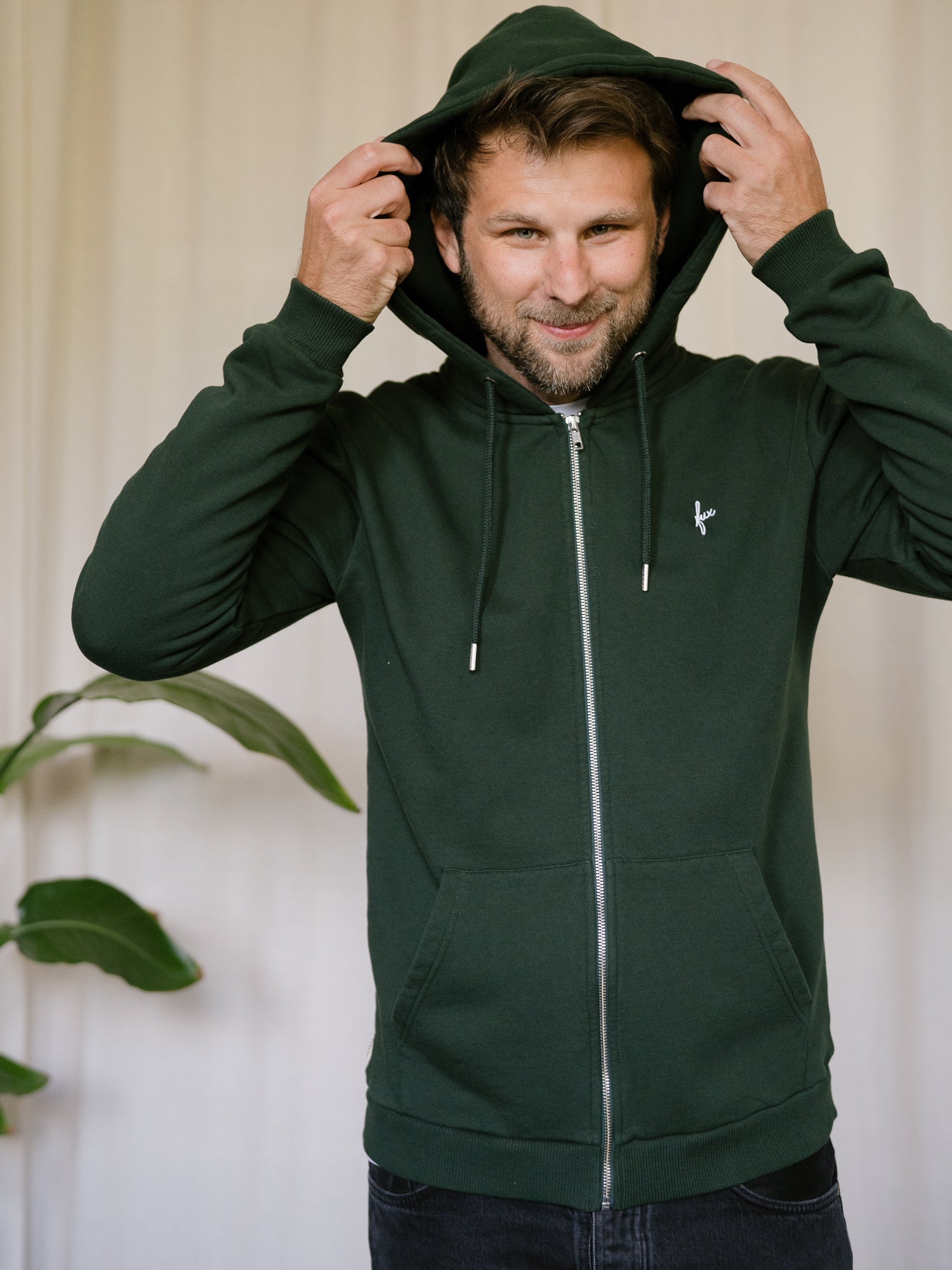 FUXBAU Sweatjacke Männer grün – Modell setzt Kapuze auf, nachhaltige Zip-Jacke aus Biobaumwolle, fair in Portugal produziert