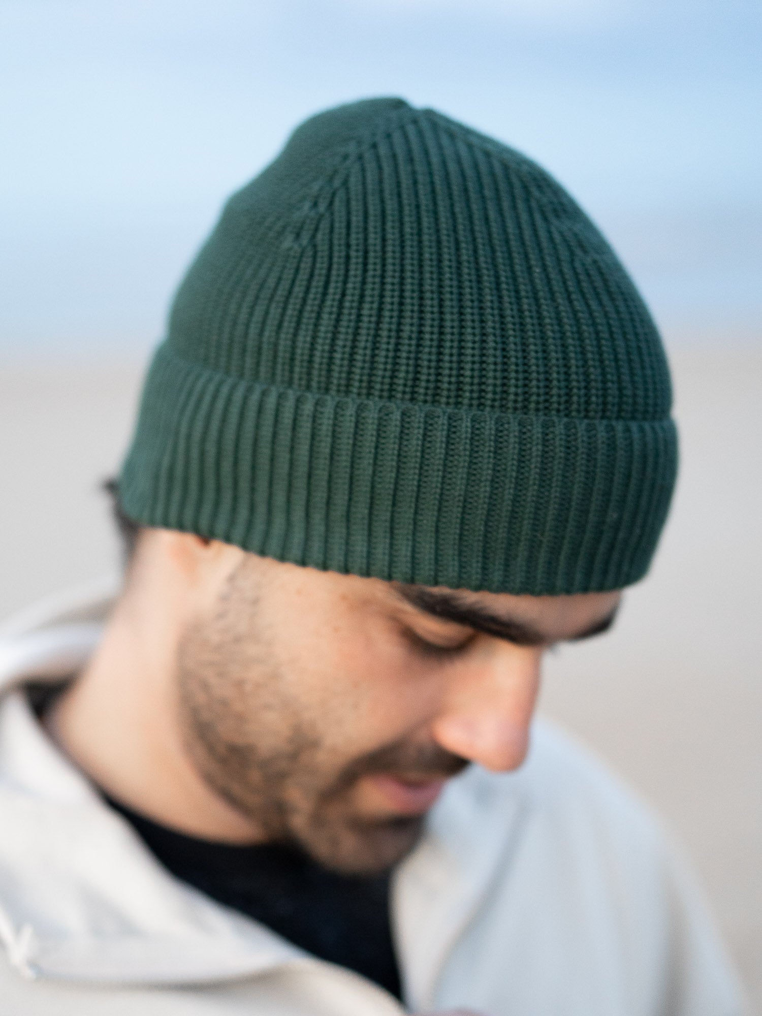 Guillermo trägt eine nachhaltige Fair Fashion Strickmütze von FUXBAU in grün aus 100% GOTS zertifizierter Biobaumwolle. Gestrickt in Italien.
