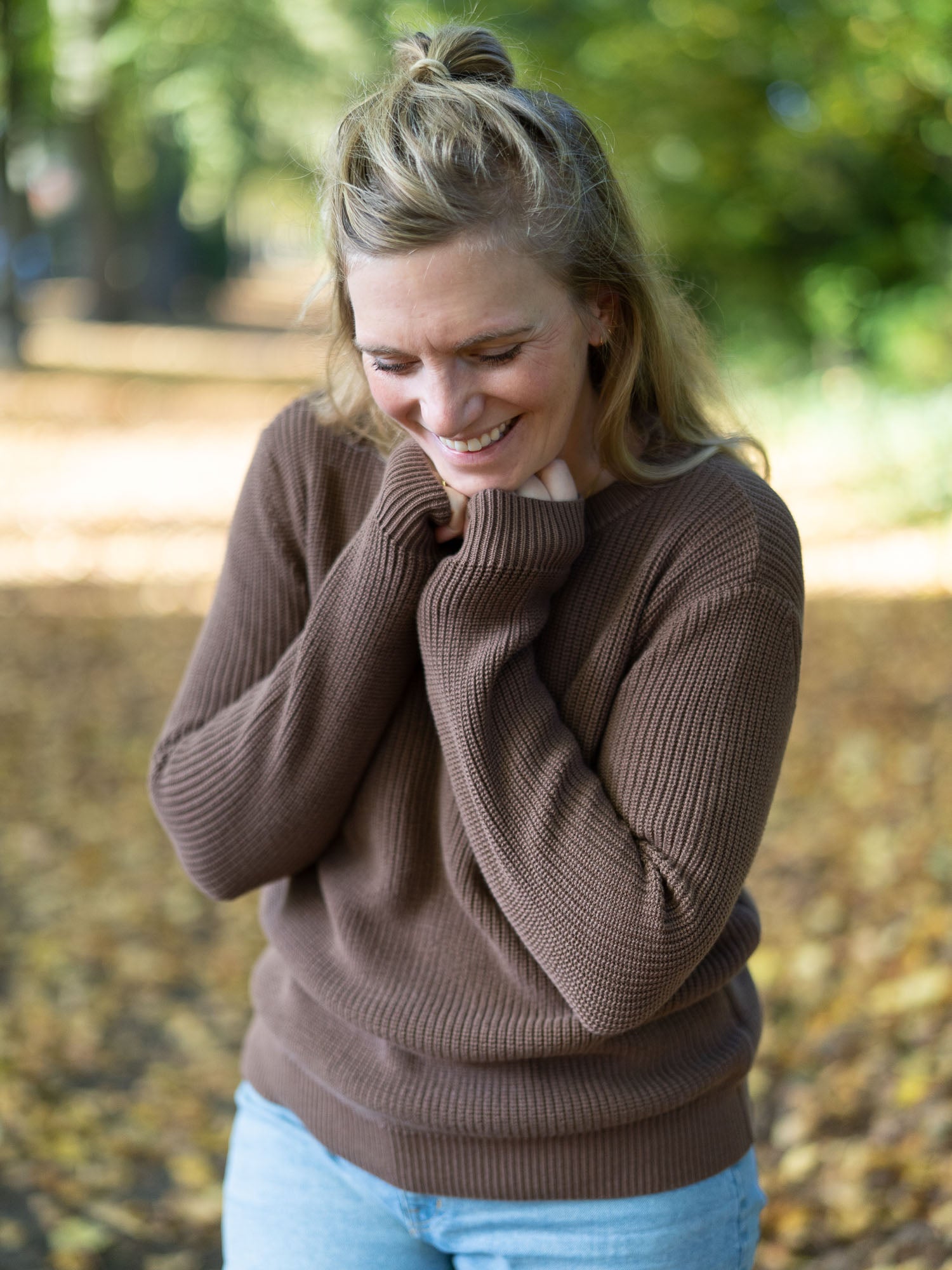 Nachhaltiger Fair Fashion 4Seasons Strickpullover aus 100% GOTS zertifizierter Biobaumwolle in braun. Getragen von einer jungen blonden Frau im Herbst.