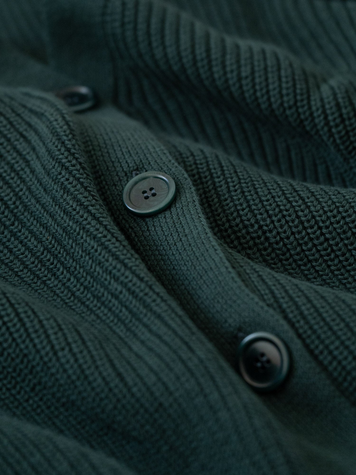 Detailansicht eines Knopfleiste von einer nachhaltigen FUXBAU Fair Fashion Strickjacke gefertigt in Italien in dunkelgrün.