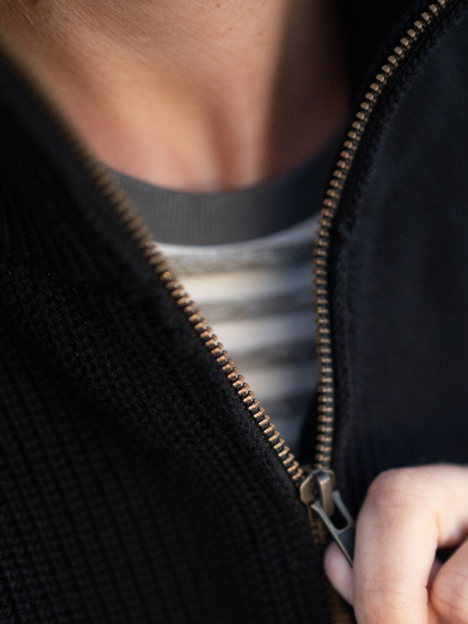 Eine junge, blonde Frau trägt einen nachhaltigen Fair Fashion 4Seasons Troyer aus Biobaumwolle Made in Italy vom nachhaltigen Fair Fashion Label FUXBAU am Strand in Portugal. Detailansicht vom YKK Reissverschluss.