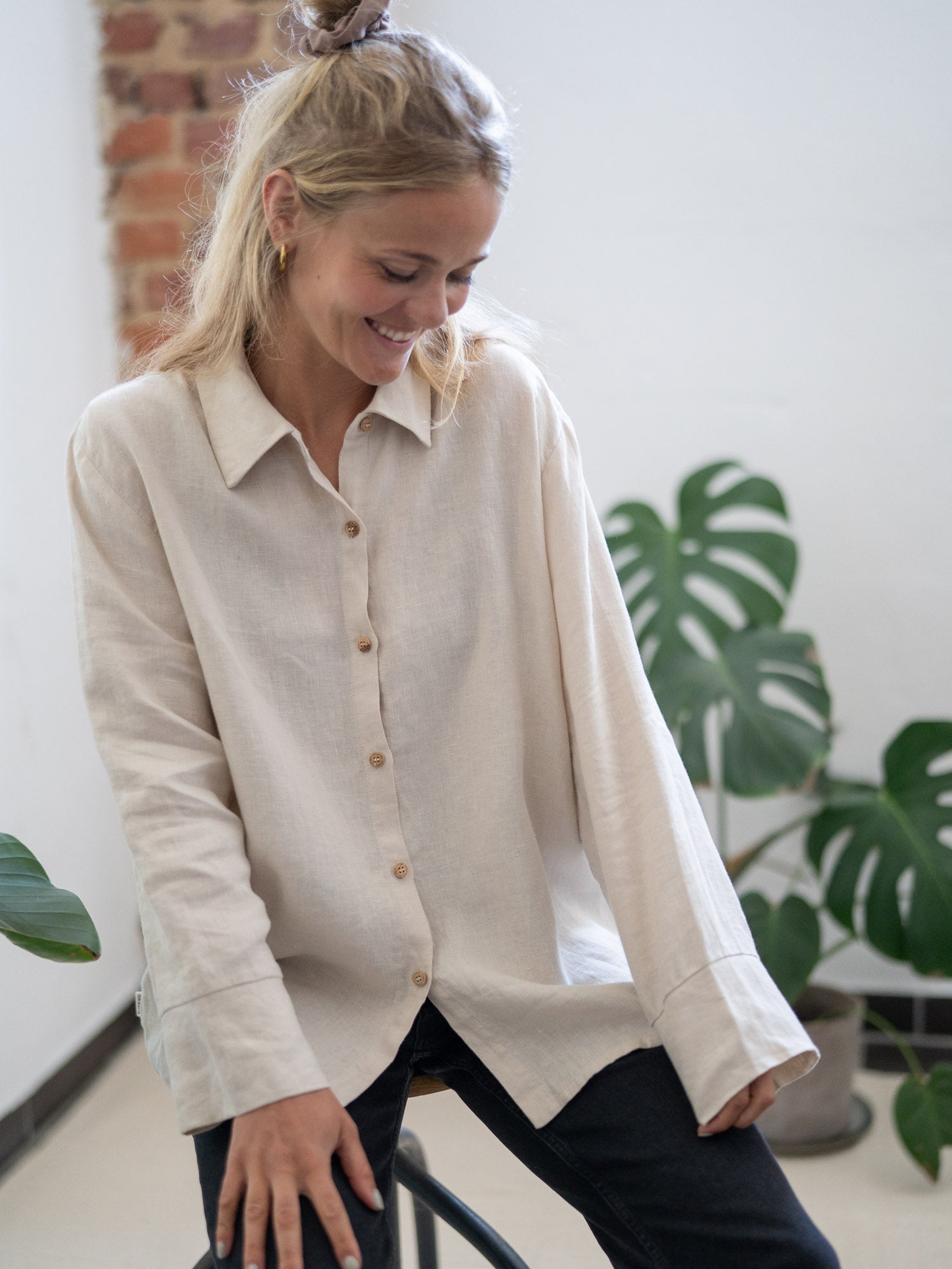 Nachhaltige Fair Fashion Frauen Leinenbluse von FUXBAU in cremeweiss aus 100% Leinen gefertigt in Portugal und fairen und nachhaltigen Bedingungen. Getragen von einer jungen, blonden Frau sitzend in Münster