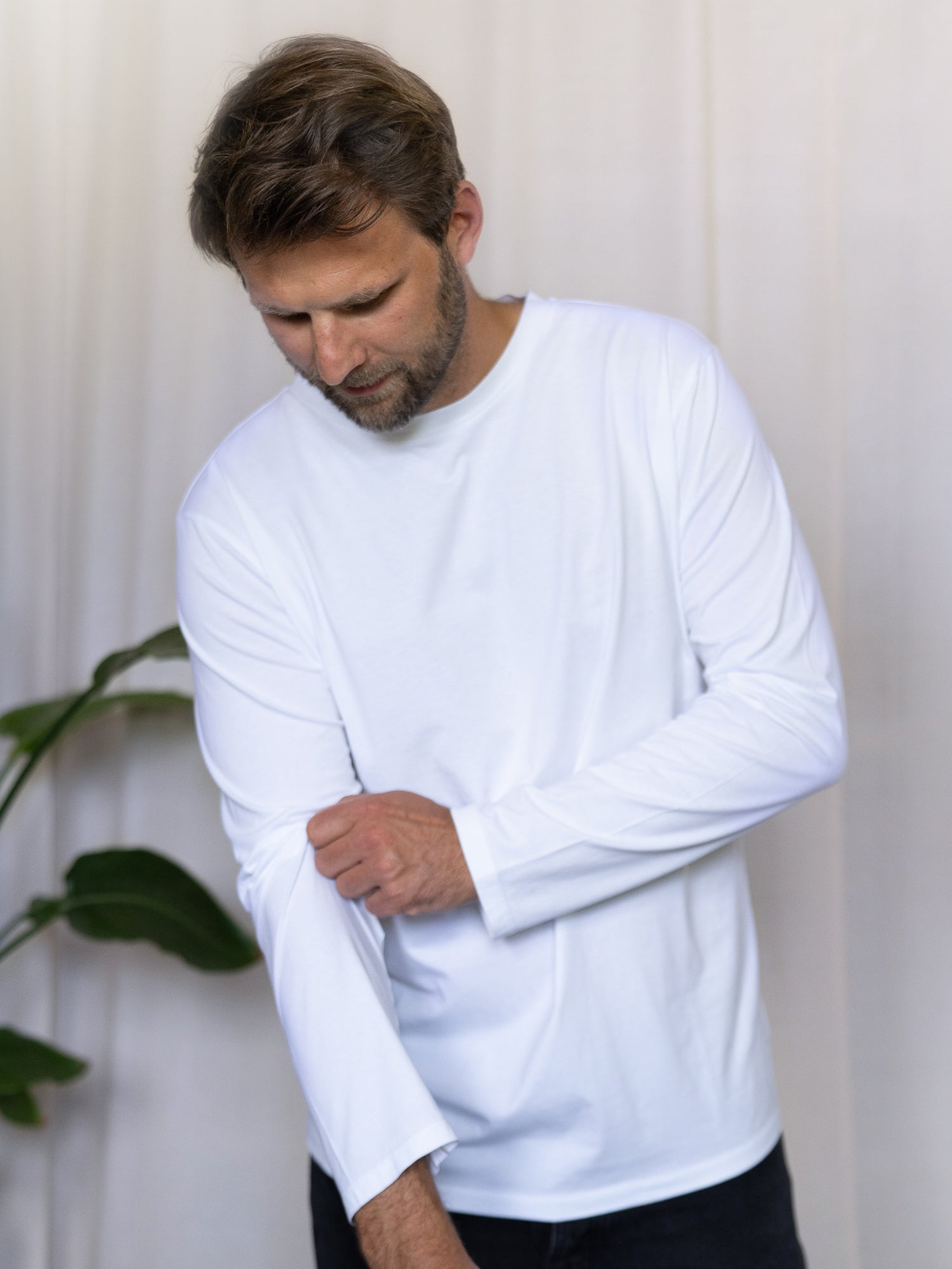 Nachhaltiges Männer Basic Langarmshirt weiß – Modell krempelt den Ärmel hoch, gefertigt aus 100% GOTS-zertifizierter Biobaumwolle in Portugal