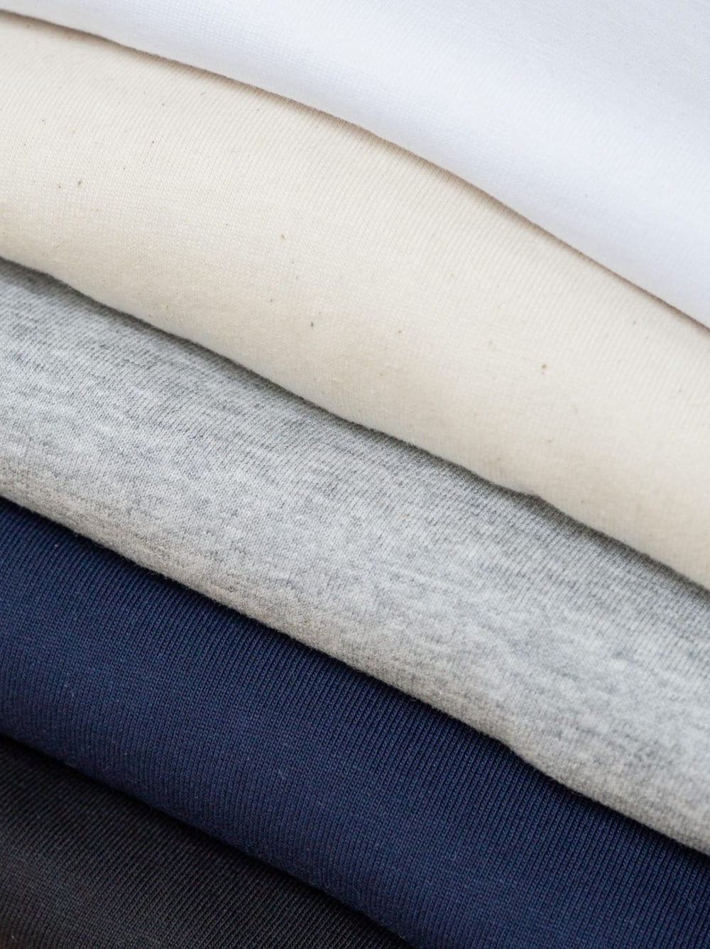 Stapel verschieden farbiger Basic T-Shirts von FUXBAU aus nachhaltiger Biobaumwolle mit einer Grammatur von 220g/m2, Spare im 3er Pack.