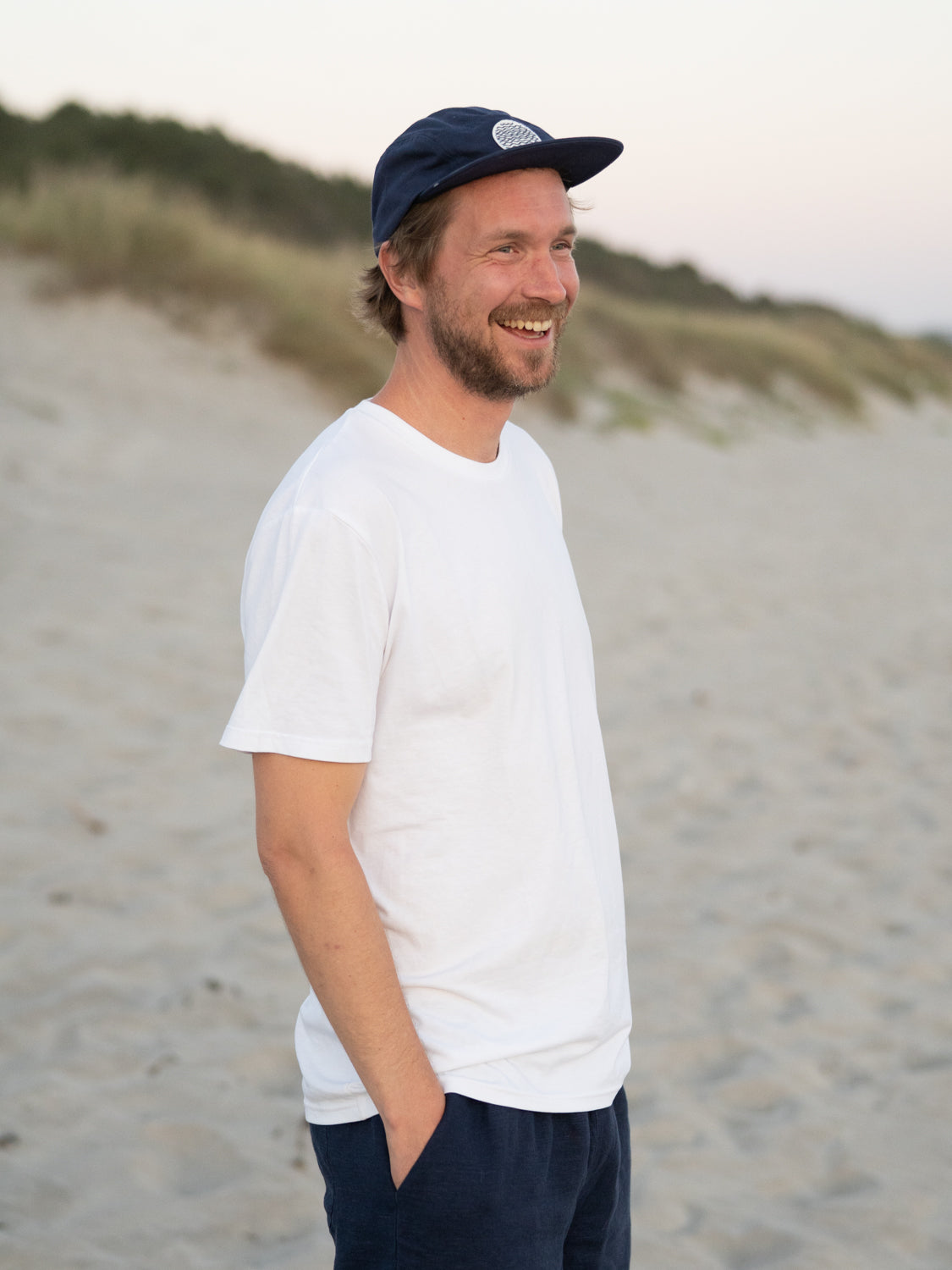 Unser Freund Kenny trägt unsere Fair Fashion Unisex Standard Basic T-Shirt in weiß aus 100% Biobaumwolle am Strand. 