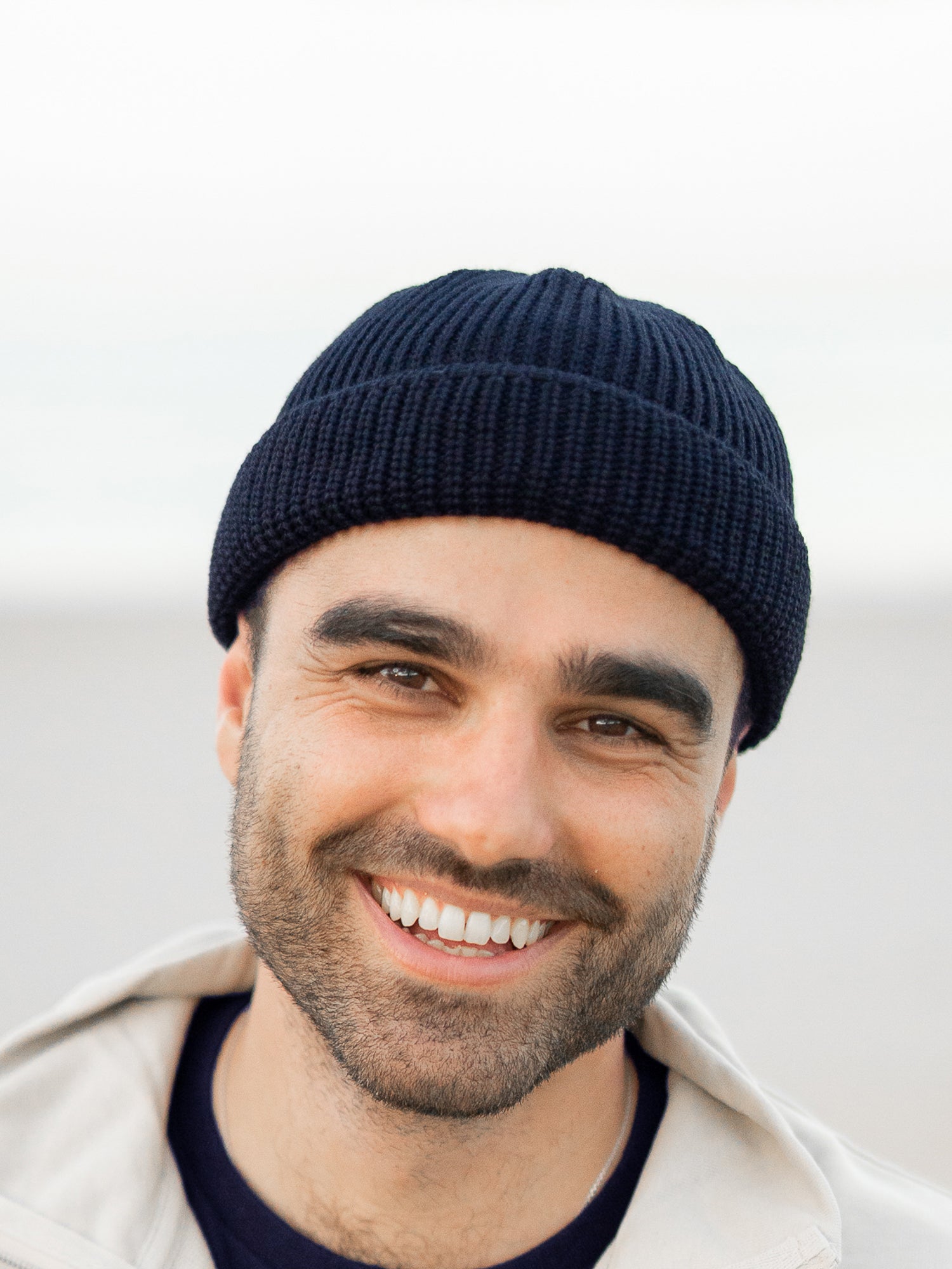 Mann trägt navyblaue FUXBAU Fischermütze aus Merinowolle am Strand – nachhaltig, fair gefertigte GOTS-zertifizierte Mütze gestrickt in Deutschland.