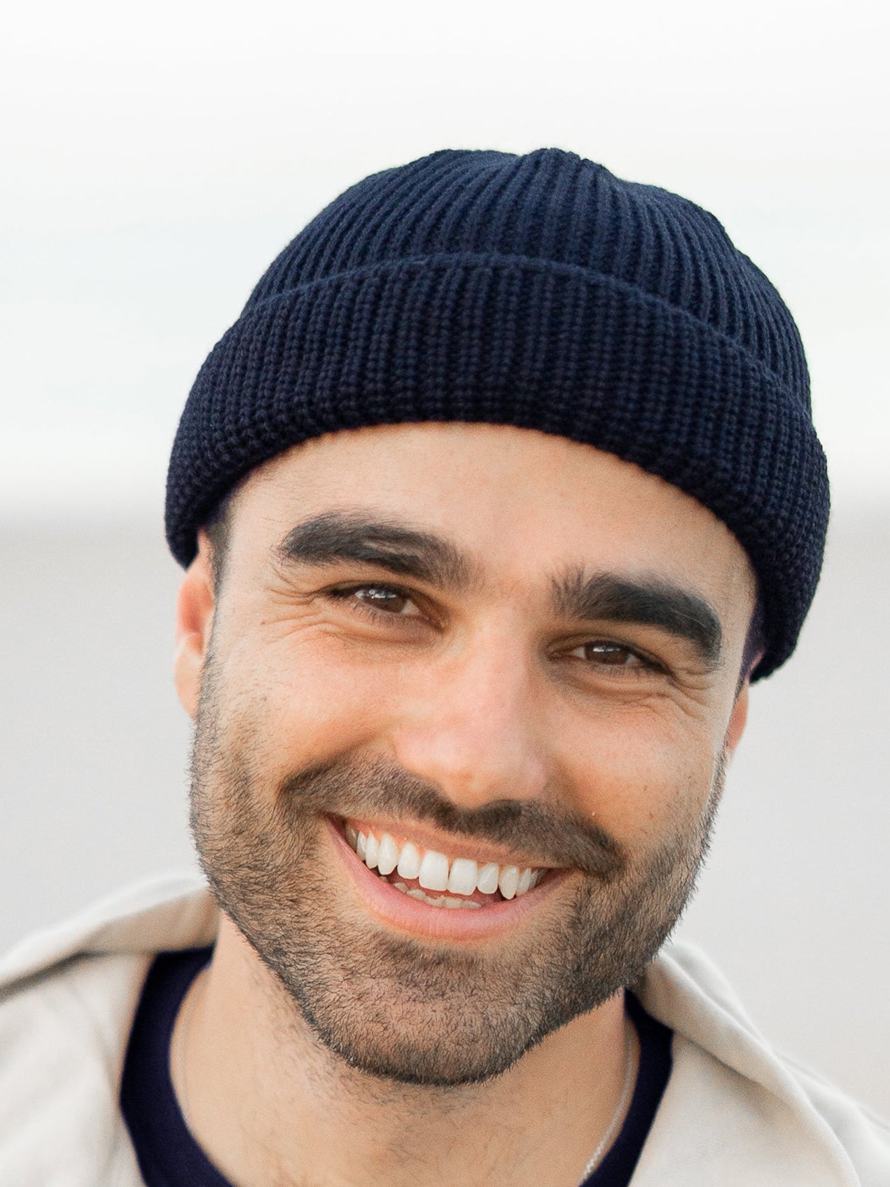 Mann trägt navyblaue FUXBAU Fischermütze aus Merinowolle am Strand – nachhaltig, fair gefertigte GOTS-zertifizierte Mütze gestrickt in Deutschland.