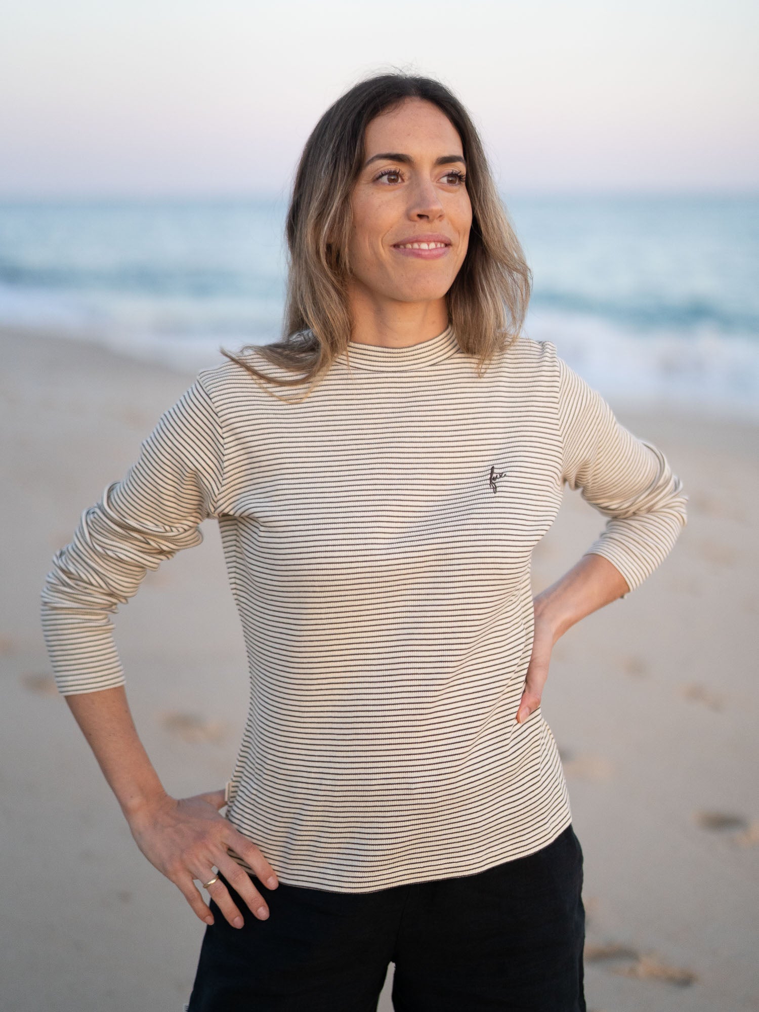 Nachhaltiges FUXBAU Fair Fashion fitted Stehkragen longsleeve creme braun gestreift aus GOTS zertifzierter Biobaumwolle Made in Portugal getragen am Strand in Portugal.