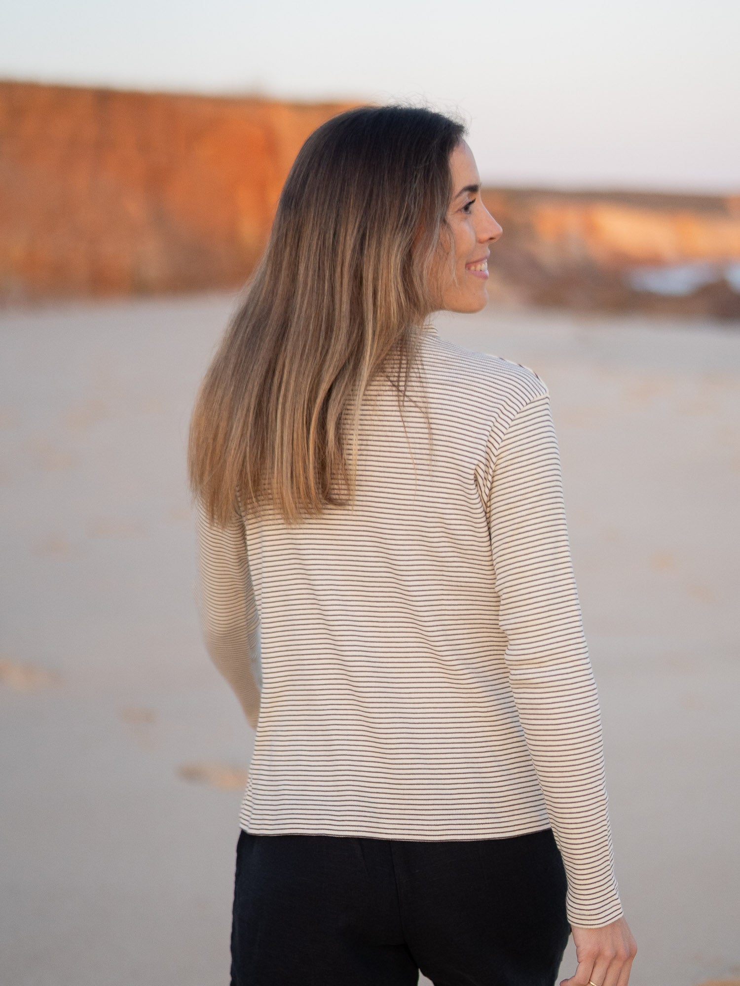 Nachhaltiges FUXBAU Fair Fashion fitted Stehkragen longsleeve creme braun gestreift aus GOTS zertifzierter Biobaumwolle Made in Portugal getragen am Strand in Portugal.