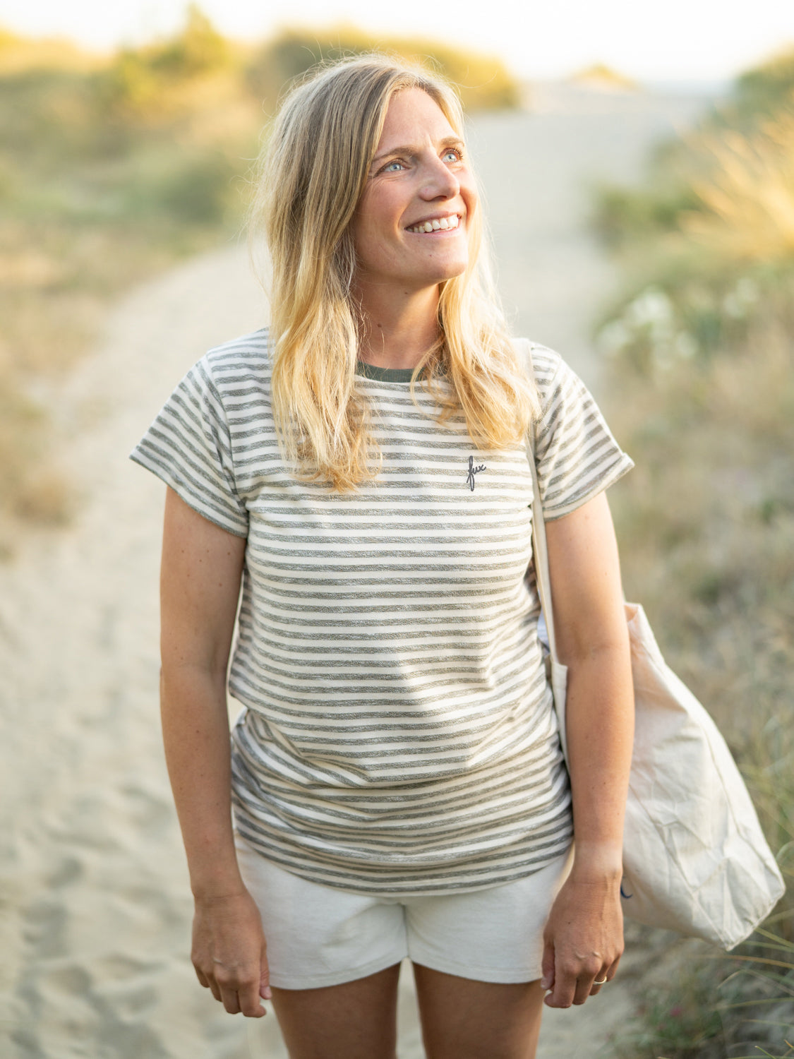 Junge, blonde Frau trägt ein FUXBAU Frauen Merida fux T-Shirt in beige grünmeliert am Strand in Portugal.