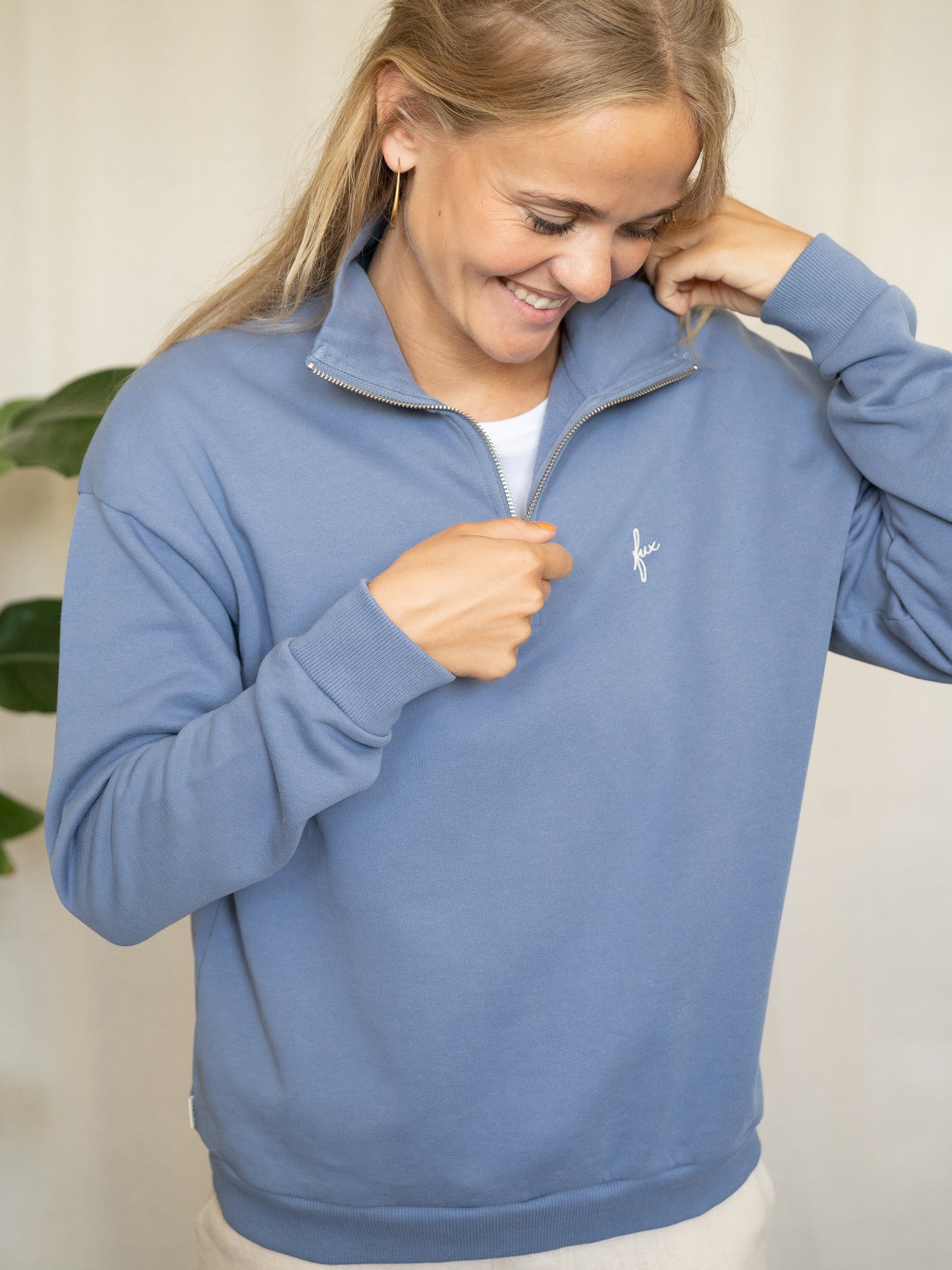 Frau trägt himmelblauen Half-Zip-Sweater aus Biobaumwolle, leicht geöffnet am Kragen