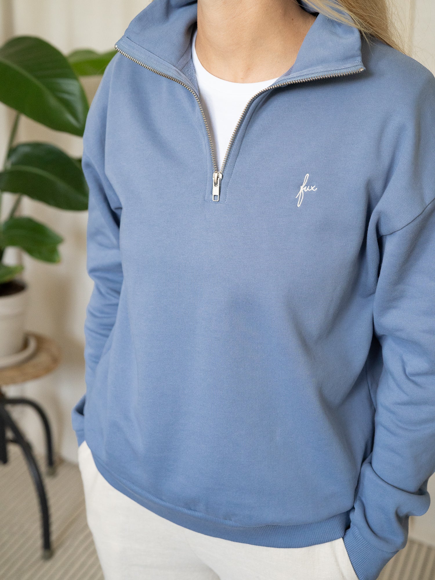 Himmelblauer Half-Zip-Sweater aus Biobaumwolle in Kombination mit weißem Shirt und heller Hose