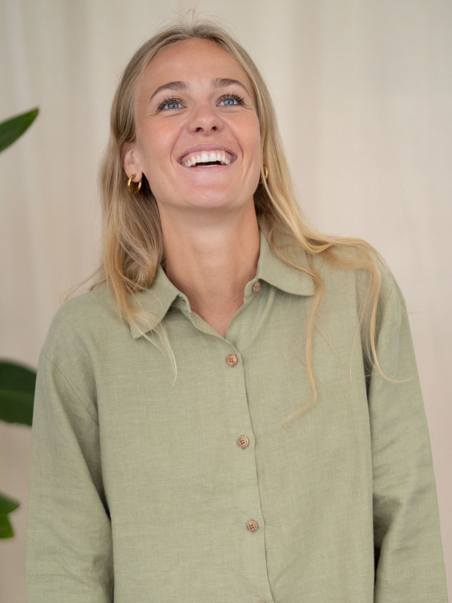 Eine junge, blonde Frau lächelt strahlend in die Kamera und trägt eine nachhaltige Frauen Langarm Leinenbluse aus 100% Leinen. Made in Portugal fair und nachhaltiger in der Farbe salbei.