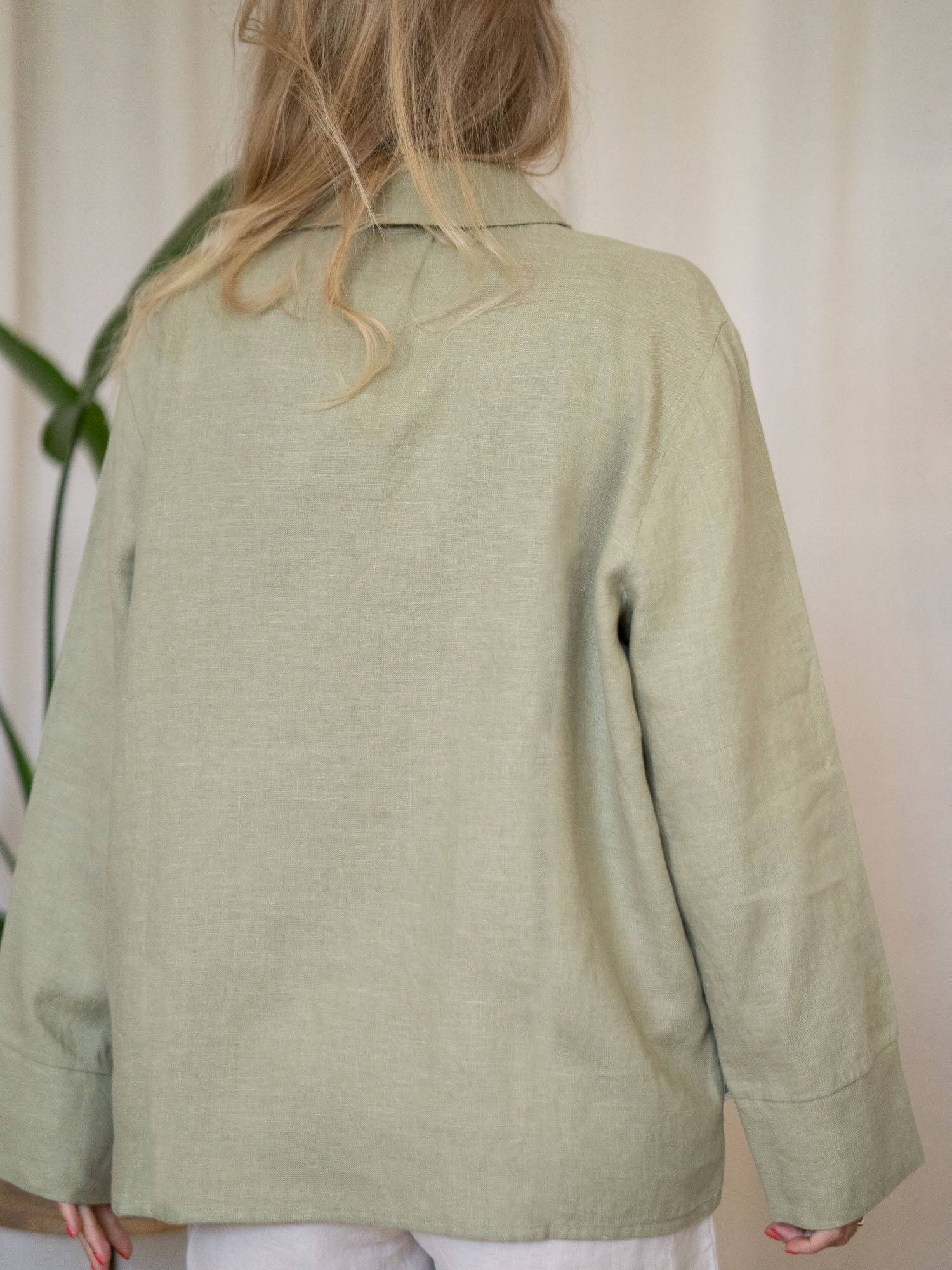 Eine junge, blonde Frau trägt eine nachhaltige Frauen Langarm Leinenbluse aus 100% Leinen vom Fair Fashion Modelabel FUXBAU. Gefertigt in Portugal unter fairen und nachhaltigen Bedingungen in der Farbe salbei.