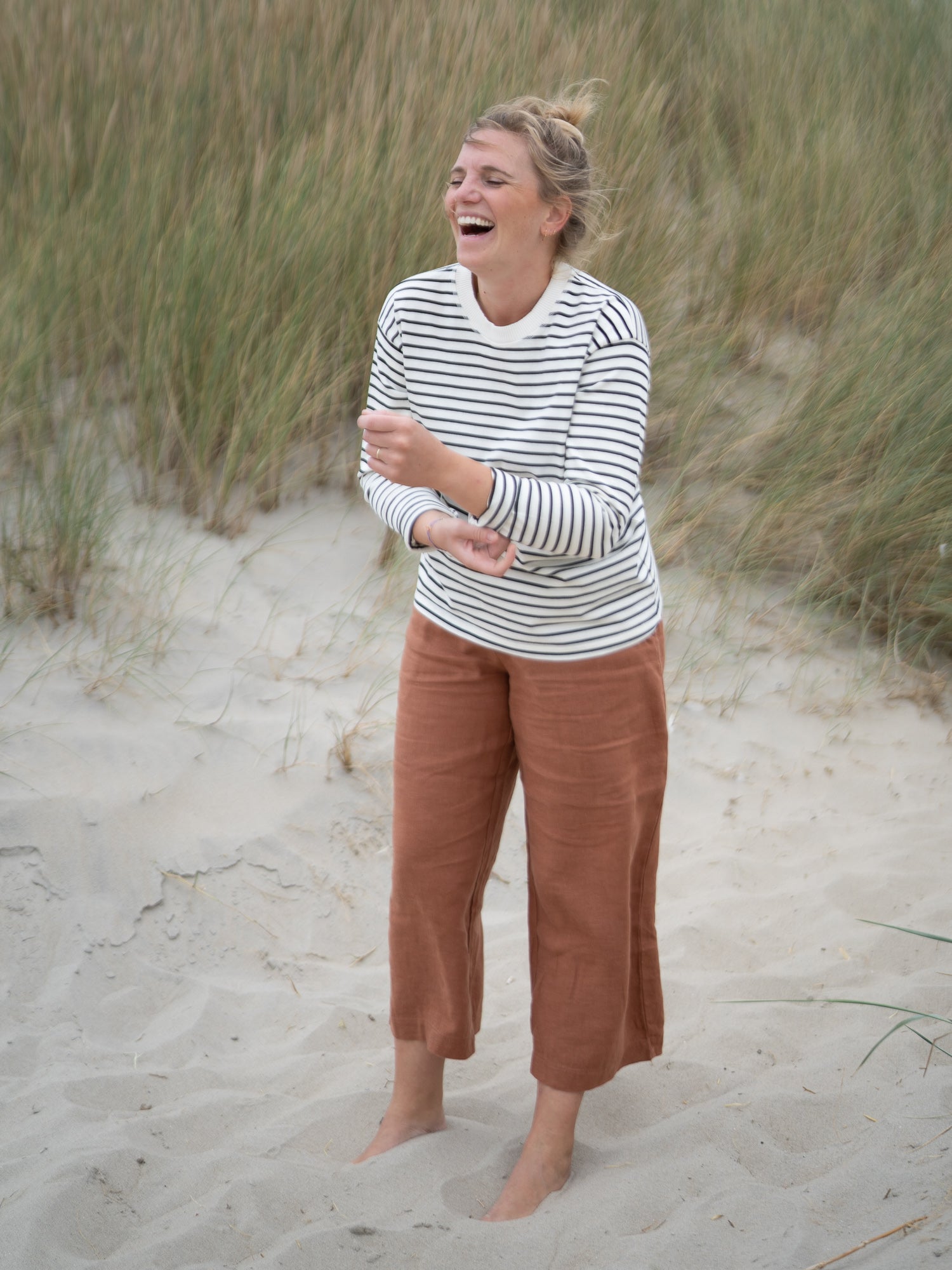 Frau trägt gestreiftes Longsleeve und nachhaltige Damen Leinenhose in Sienna Braun von FUXBAU am Strand – fair produziert in Portugal