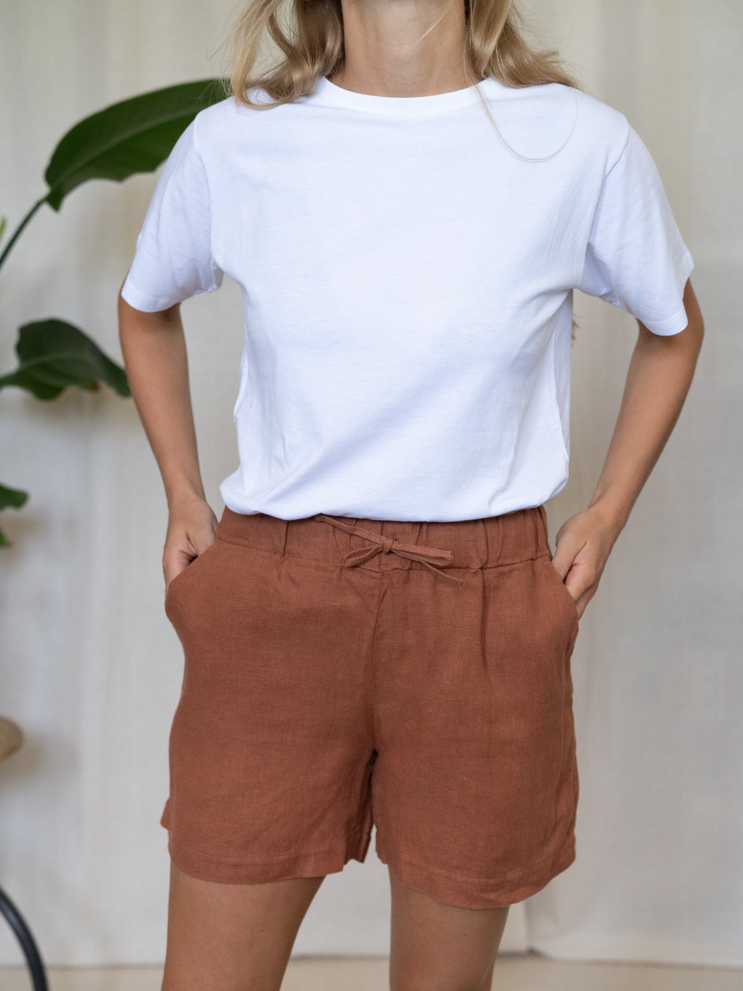 Eine junge, blonde Frau trägt eine nachhaltige Fair Fashion Frauen Leinenshorts von FUXBAU in der Farbe sienna rotbraun aus 100% Leinen.