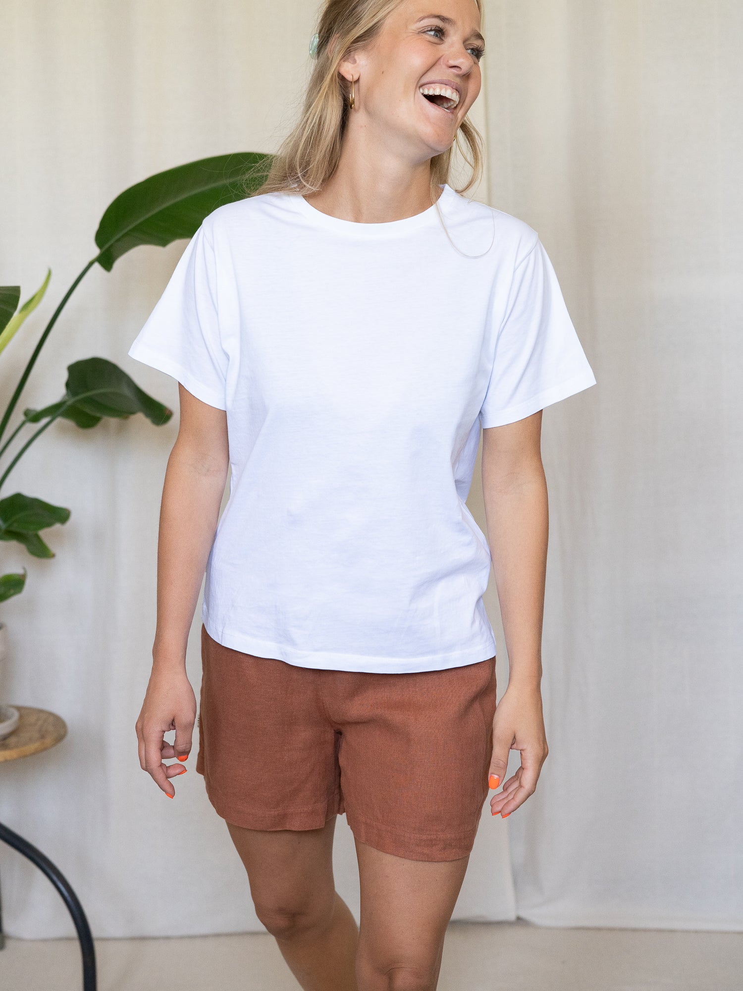 Eine junge, blonde Frau trägt eine nachhaltige Fair Fashion Frauen Leinenshorts von FUXBAU in der Farbe sienna rotbraun aus 100% Leinen.