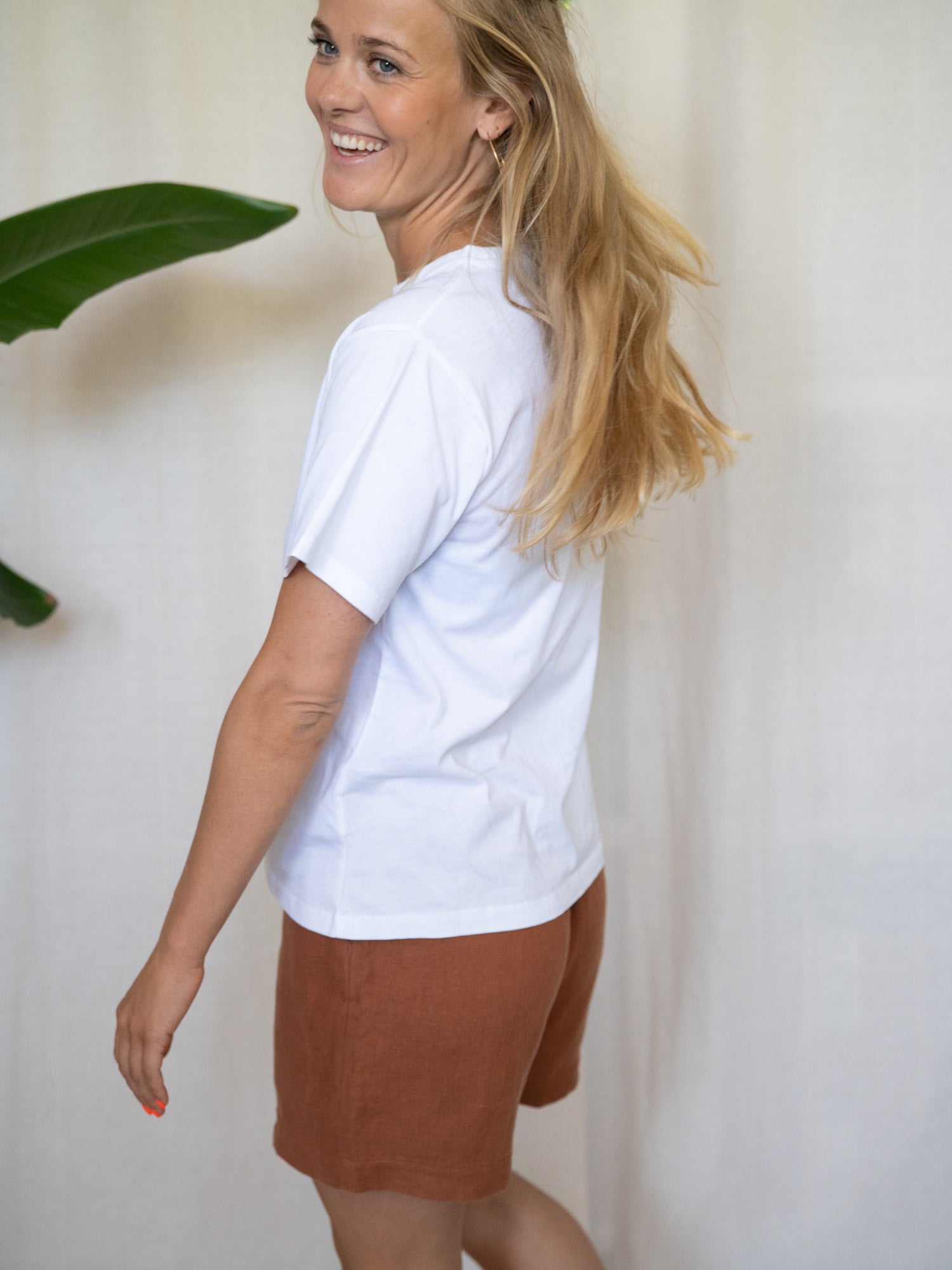 Eine junge, blonde Frau trägt eine nachhaltige Fair Fashion Frauen Leinenshorts von FUXBAU in der Farbe sienna rotbraun aus 100% Leinen.