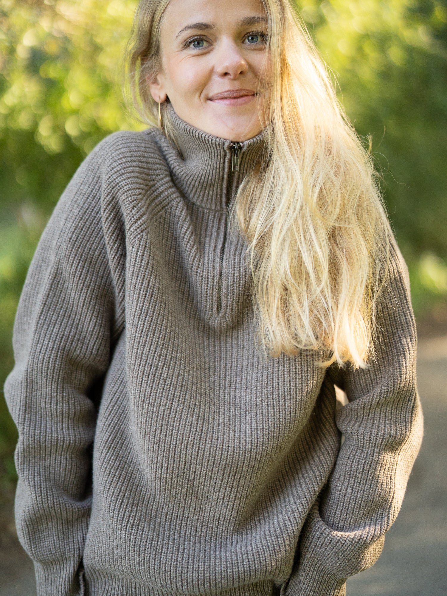 Nachhaltiger Fair Fashion Frauen Merino Troyer in braun meliert aus 100% Merino Schurwolle Made in Italy, getragen von einer jungen Frau, die in die Kamera frontal lächelt.