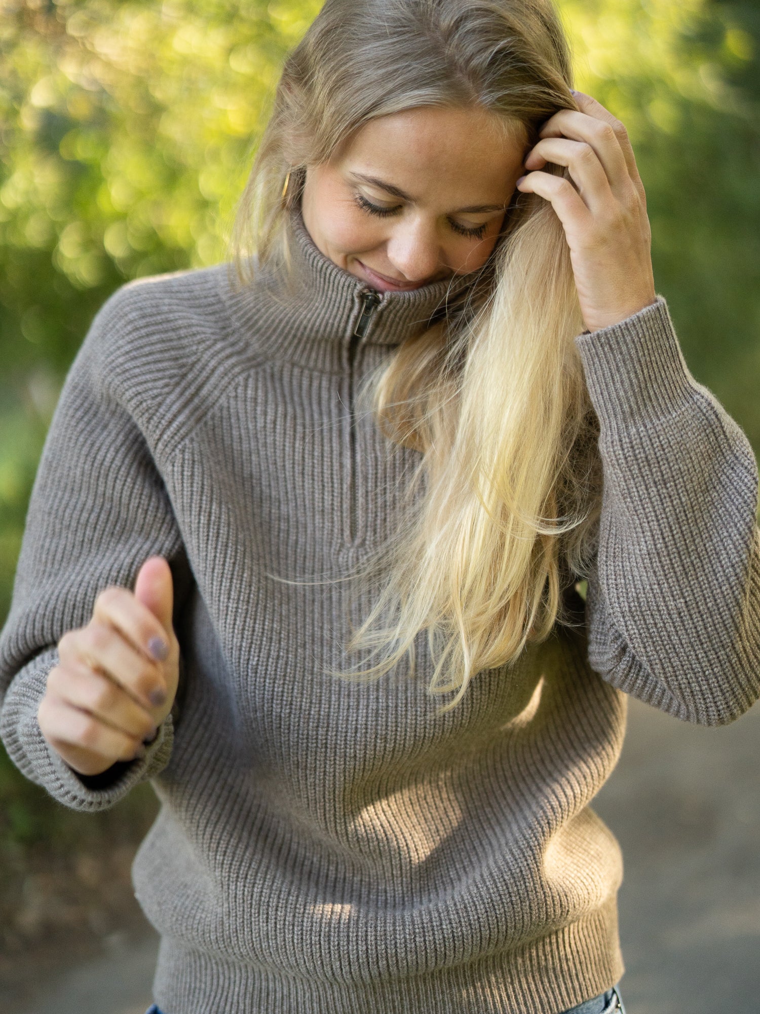Nachhaltiger Fair Fashion Frauen Merino Troyer in braun meliert aus 100% Merino Schurwolle Made in Italy, getragen von einer jungen Frau, die leicht nach unten schaut und lächelt.