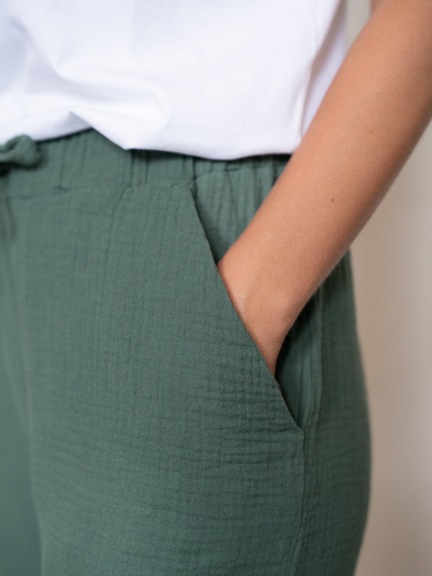 Nahaufnahme einer Hand in der Seitentasche der grünen Musselinhose aus weichem Musselin