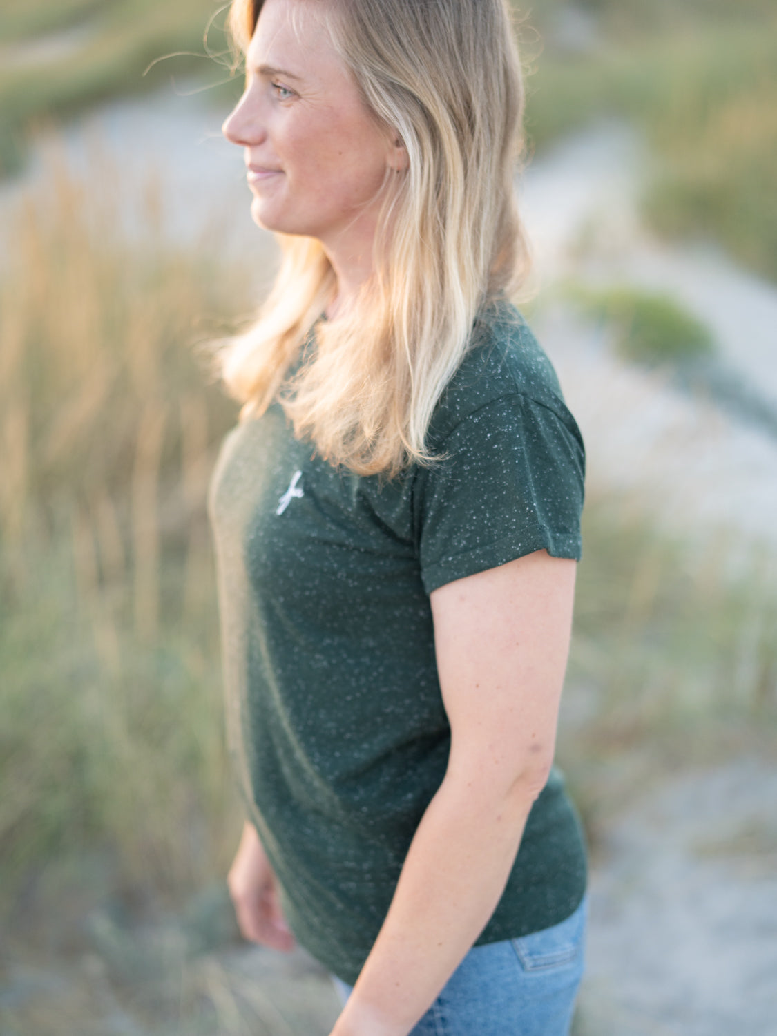 FUXBAU Fair Fashion Frauen T-Shirt in grün aus Biobaumwollen mit weißen Punkten getragen von einer jungen blonden Frau am Strand.