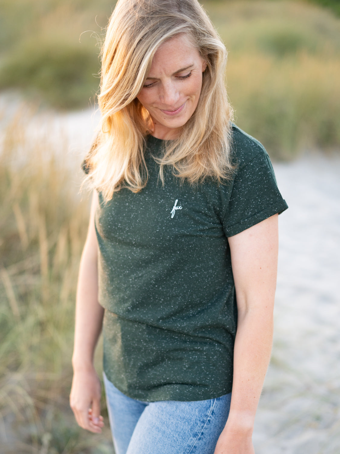 FUXBAU Fair Fashion Frauen T-Shirt in grün aus Biobaumwollen mit weißen Punkten getragen von einer jungen blonden Frau am Strand.