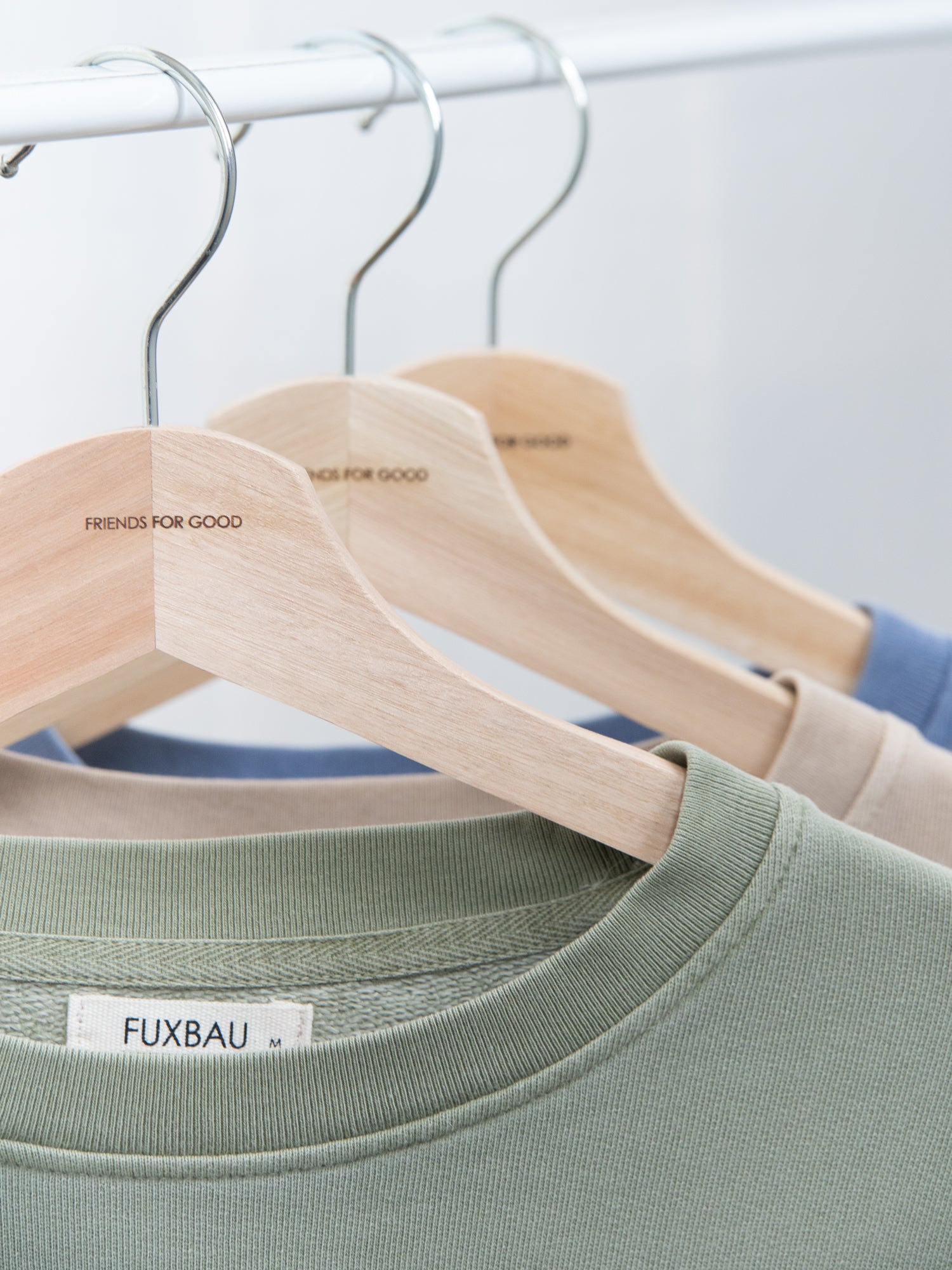 Drei verschieden farbige Fair Fashion Frauen Oversize Pullover in grün, beige und blau von FUXBAU hängen an einer Kleiderstange.
