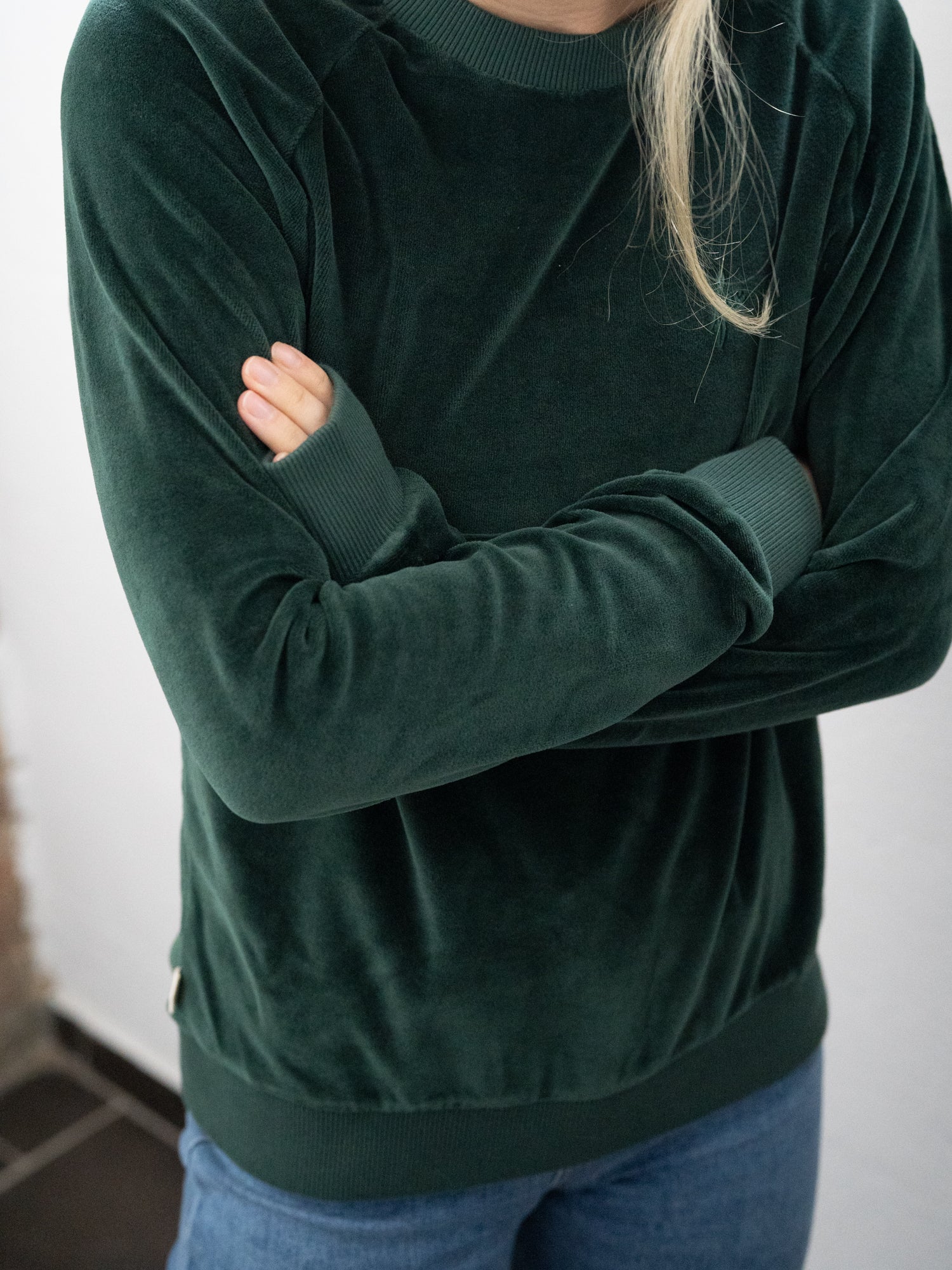 Detailansicht eines Fair Fashion FUXBAU Frauen Samt Sweater in grün aus 100% GOTS zertifizierter Biobaumwolle made in Portugal. Getragen von Greta bei uns im Ladenbüro in Münster.