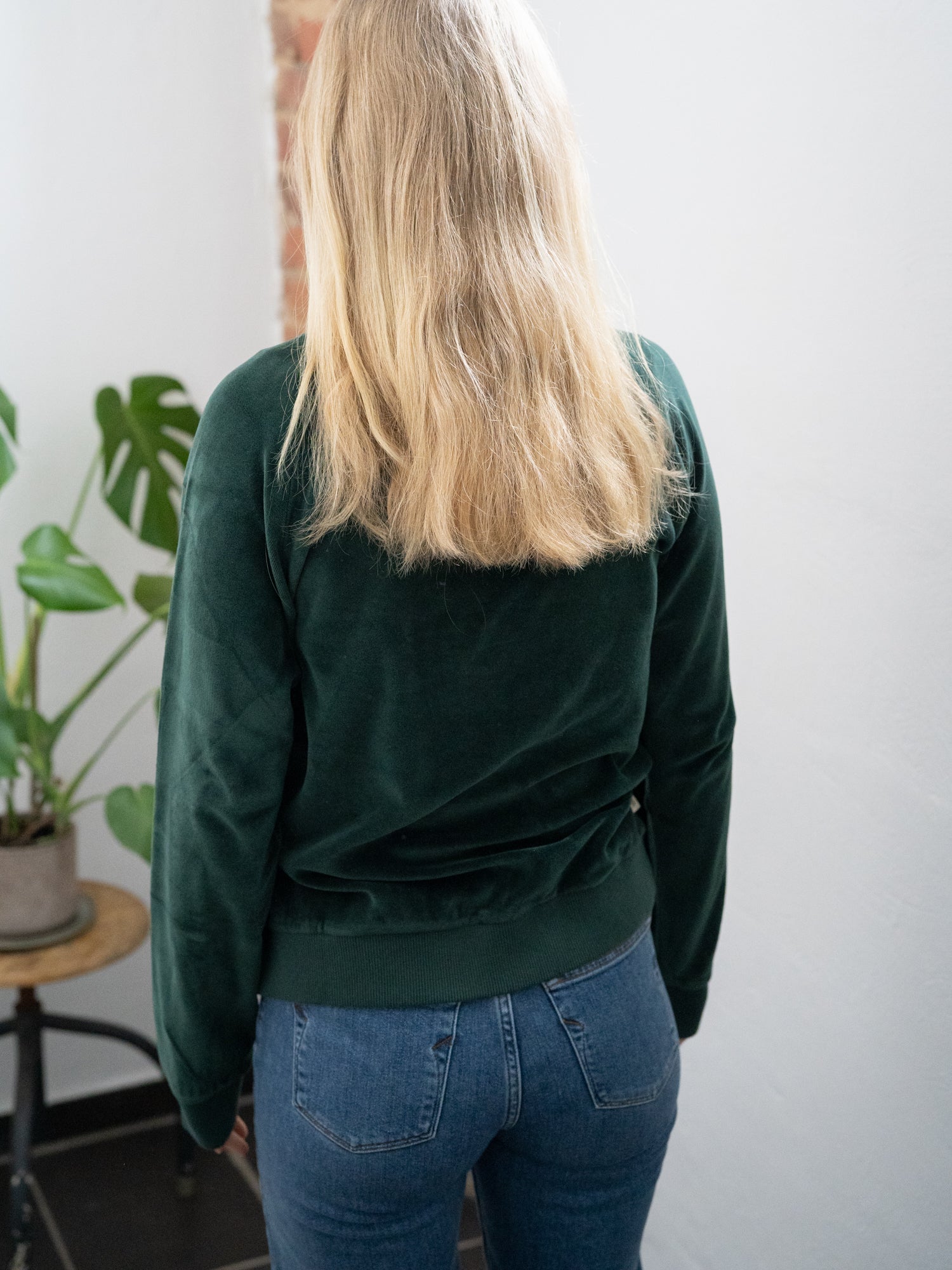 Rückansicht eines Fair Fashion FUXBAU Frauen Samt Sweater in grün aus 100% GOTS zertifizierter Biobaumwolle made in Portugal. Getragen von Greta bei uns im Ladenbüro in Münster.