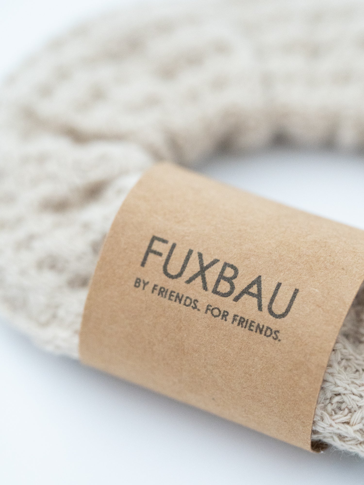 Nahaufnahme eines beigen FUXBAU Waffelstrick-Scrunchies mit Papierbanderole – fair produziert, nachhaltig und stilvoll.