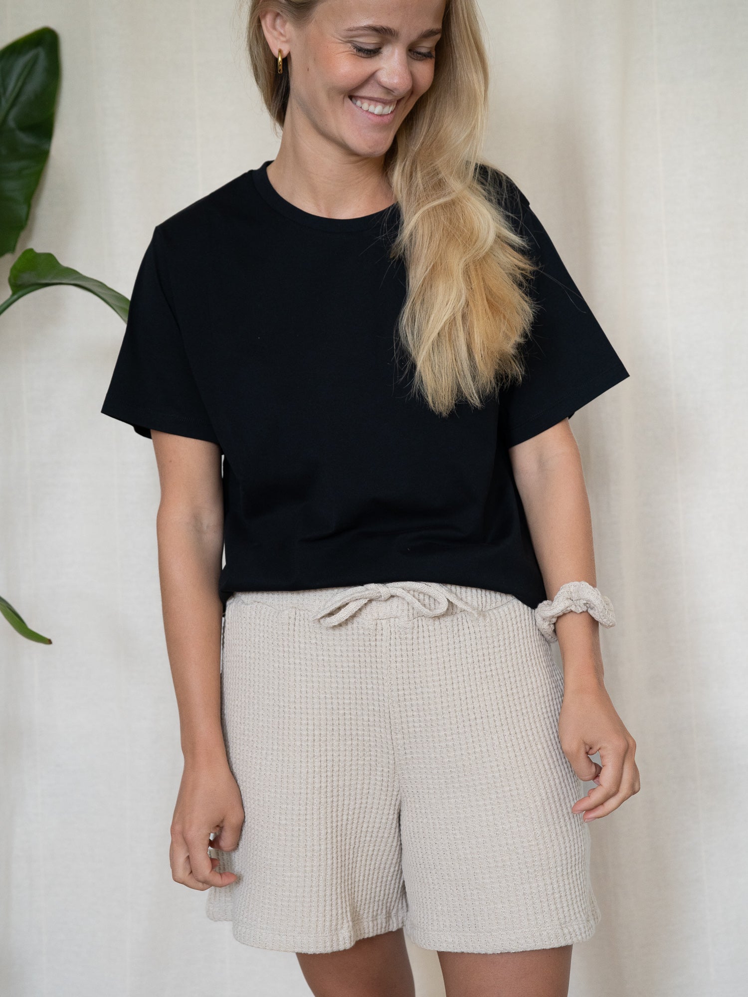 Alt-Text: Lächelnde Frau trägt nachhaltige Waffelstrick Shorts für Damen in Beige – Fair Fashion Look mit schwarzem T-Shirt