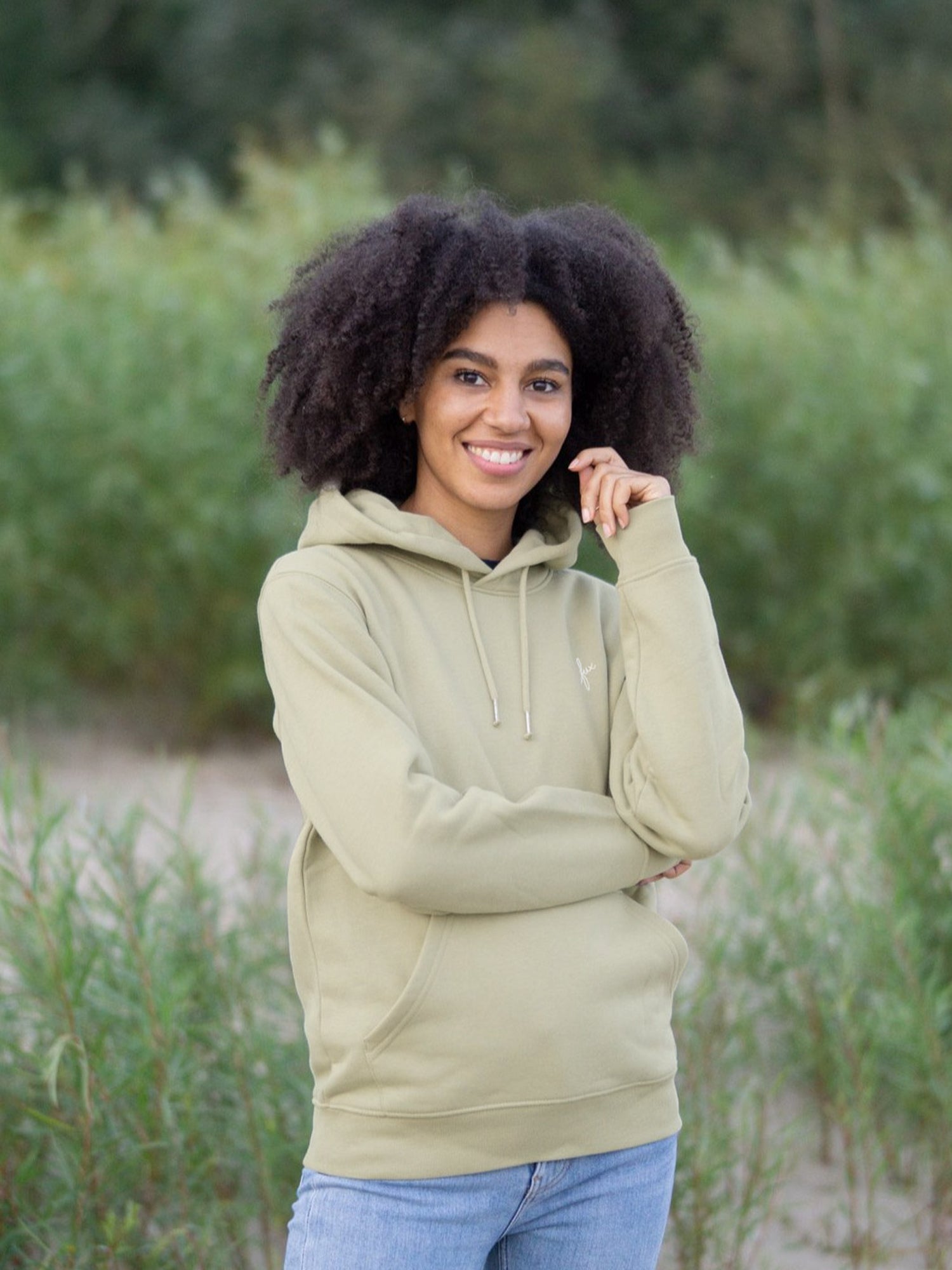 Eine junge, schwarzhaarige Frau trägt einen nachhaltigen Hoodie von FUXBAU in salbei grün.
