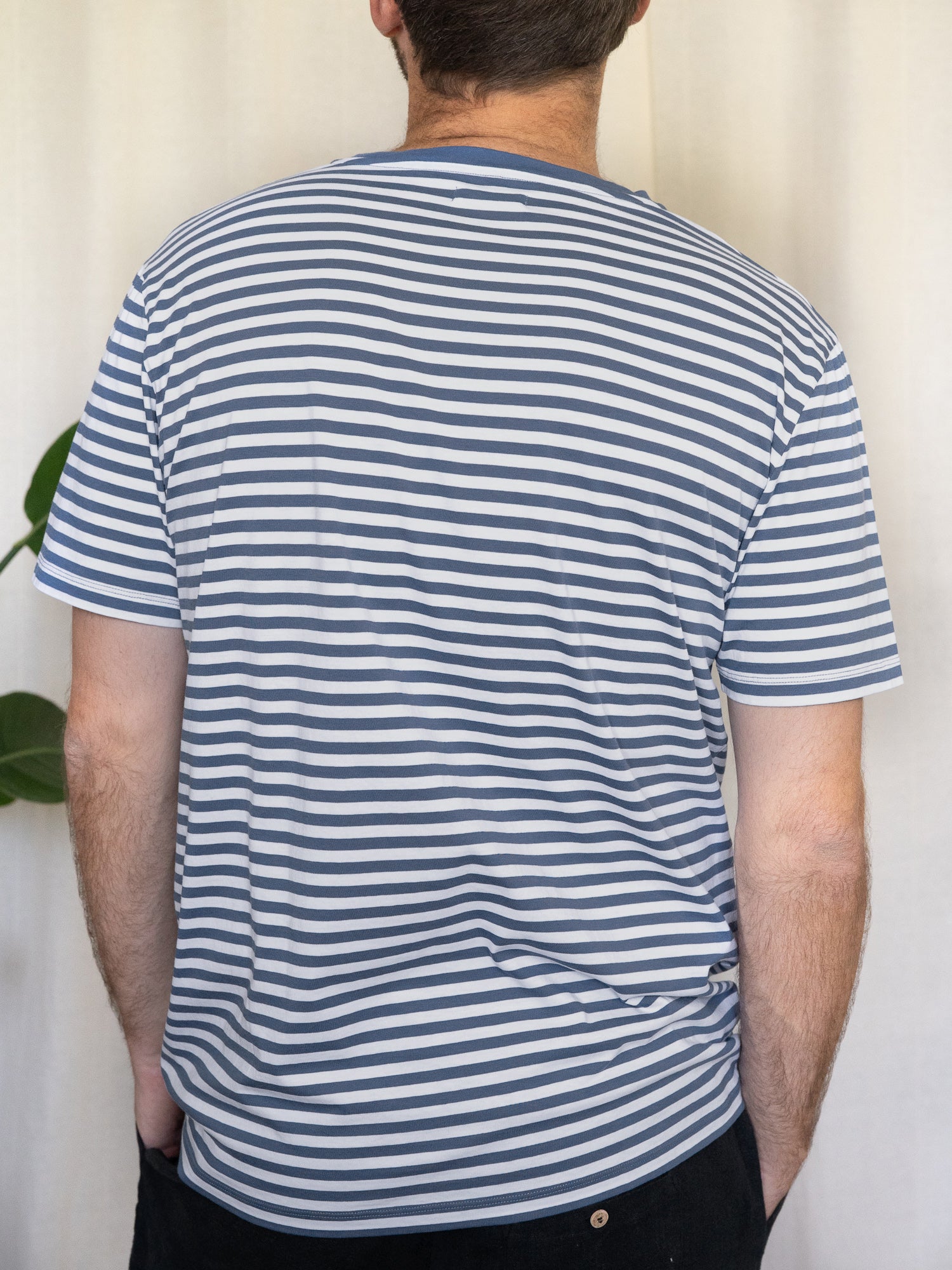 Rückansicht von einem gestreiften Fair Fashion T-Shirt von FUXBAU für Männer in blau weiss aus 100% Biobaumwolle. Getragen von einem jungen Mann.