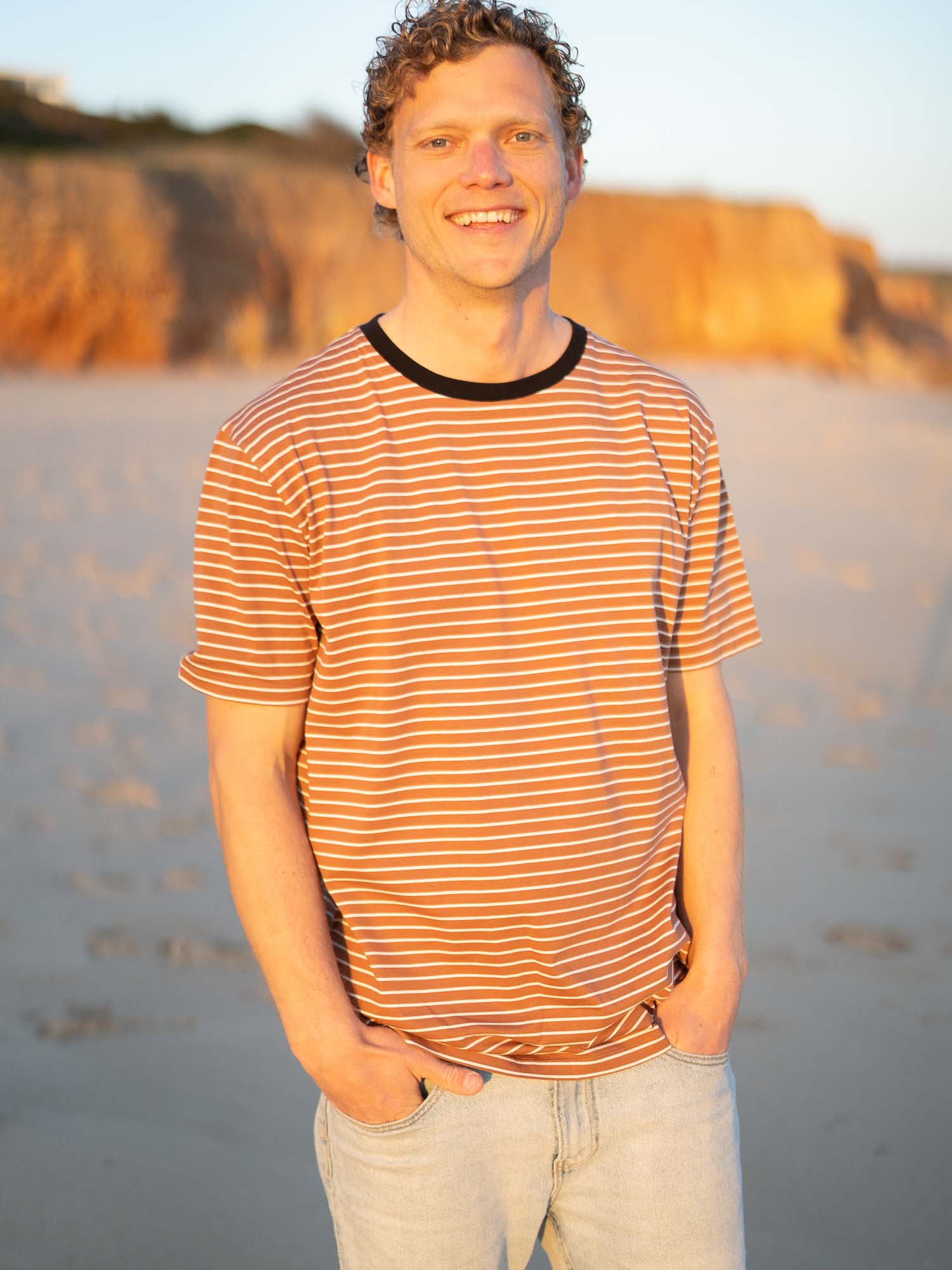 Gestreiftes Fair Fashion T-Shirt in karamell, schwarz und weiss von FUXBAU aus Biobaumwolle. Gefertigt unter nachhaltigen GOTS Bedingungen in Portugal und getragen am Strand in Portugal.