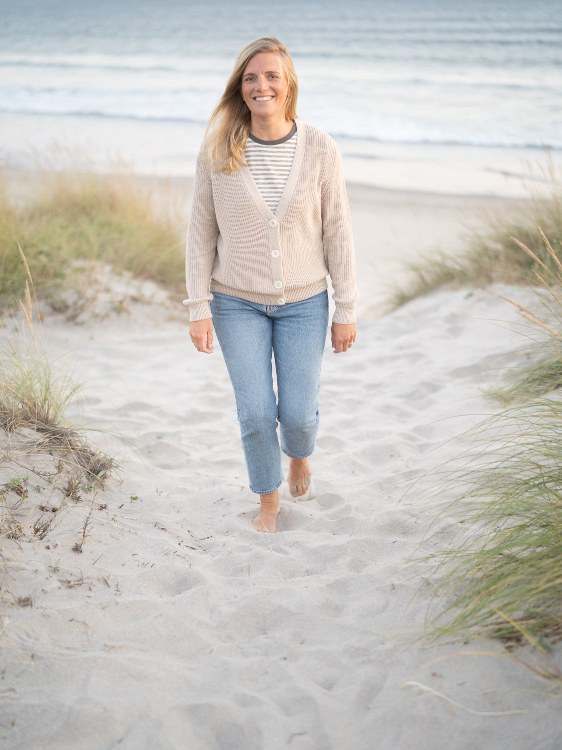 FUXBAU 4Seasons Frauen Strickjacke in beigemeliert aus 100% GOTS zertifizierter Biobaumwolle. Gefertigt in Italien und gertragen von einer jungen Frau am Strand in Portugal.