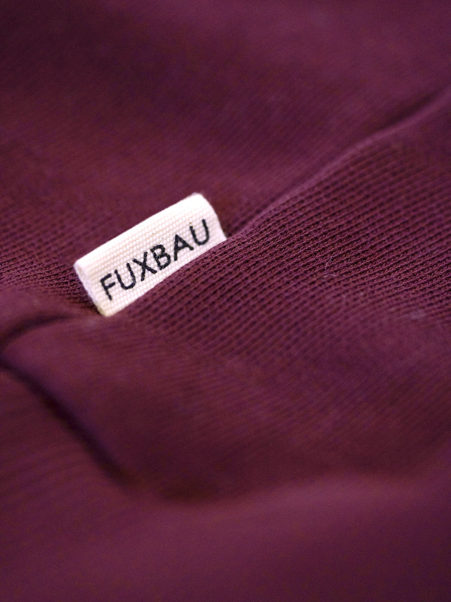 Seitliches FUXBAU Label auf nachhaltigem Half Zip Sweater aus Bio-Baumwolle in Bordeaux – hochwertige Verarbeitung, fair gefertigt in Portugal.