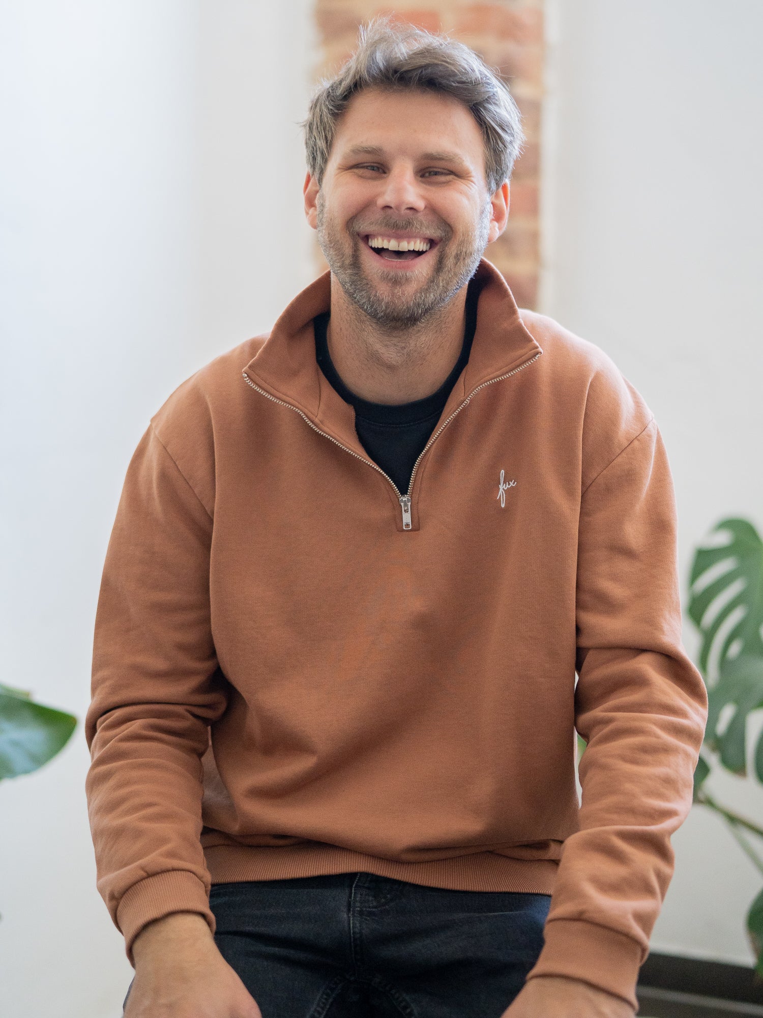 Nachhaltiger Fair Fashion Männer Half Zip Sweater in Karamell von FUXBAU. Gefertigt aus 100% GOTS zertifizierter Biobaumwolle in Portugal. Getragen von einem jungen, blonden Mann.