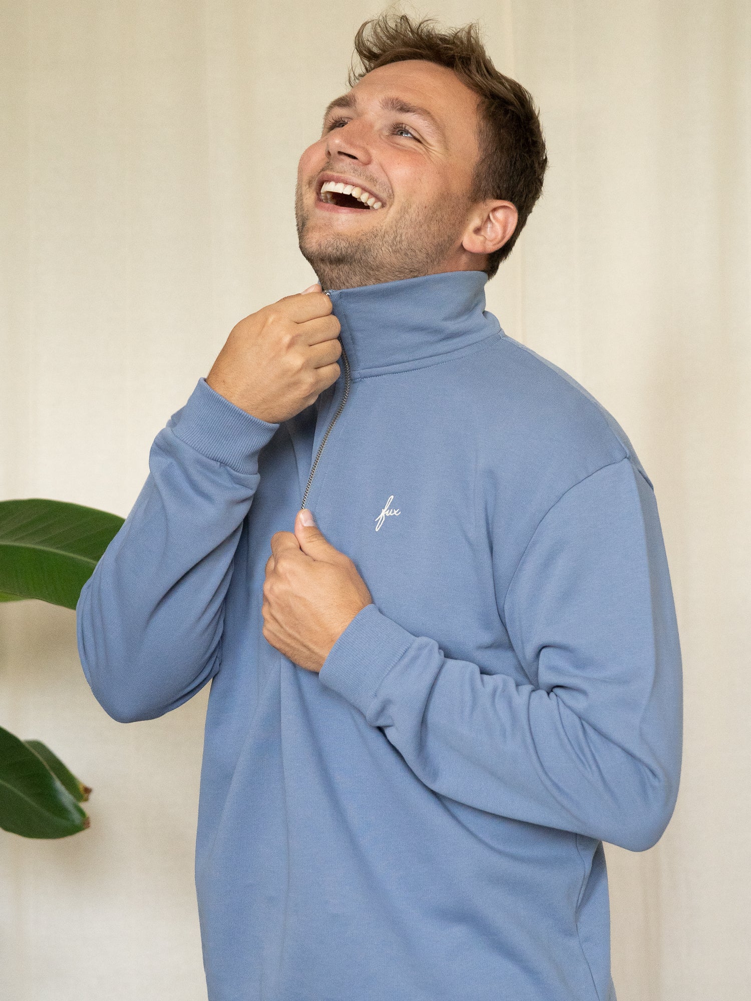 Mann zieht den Kragen des Half-Zip Sweaters hoch, lacht und schaut nach oben.