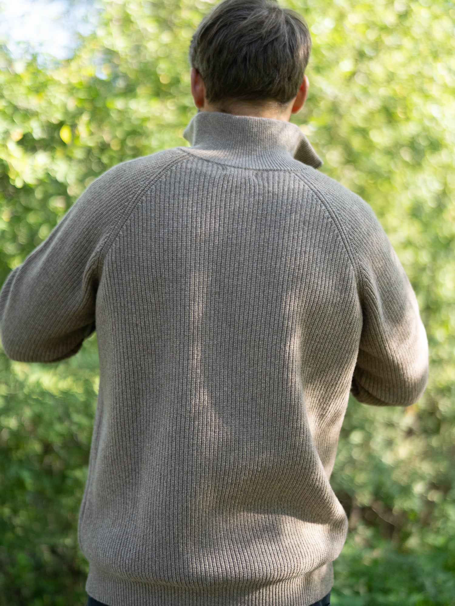 Nachhaltiger Fair Fashion Männer Merino Troyer in braun meliert aus 100% Merino Schurwolle Made in Italy, getragen von einem jungen Mann mit Rückansicht.