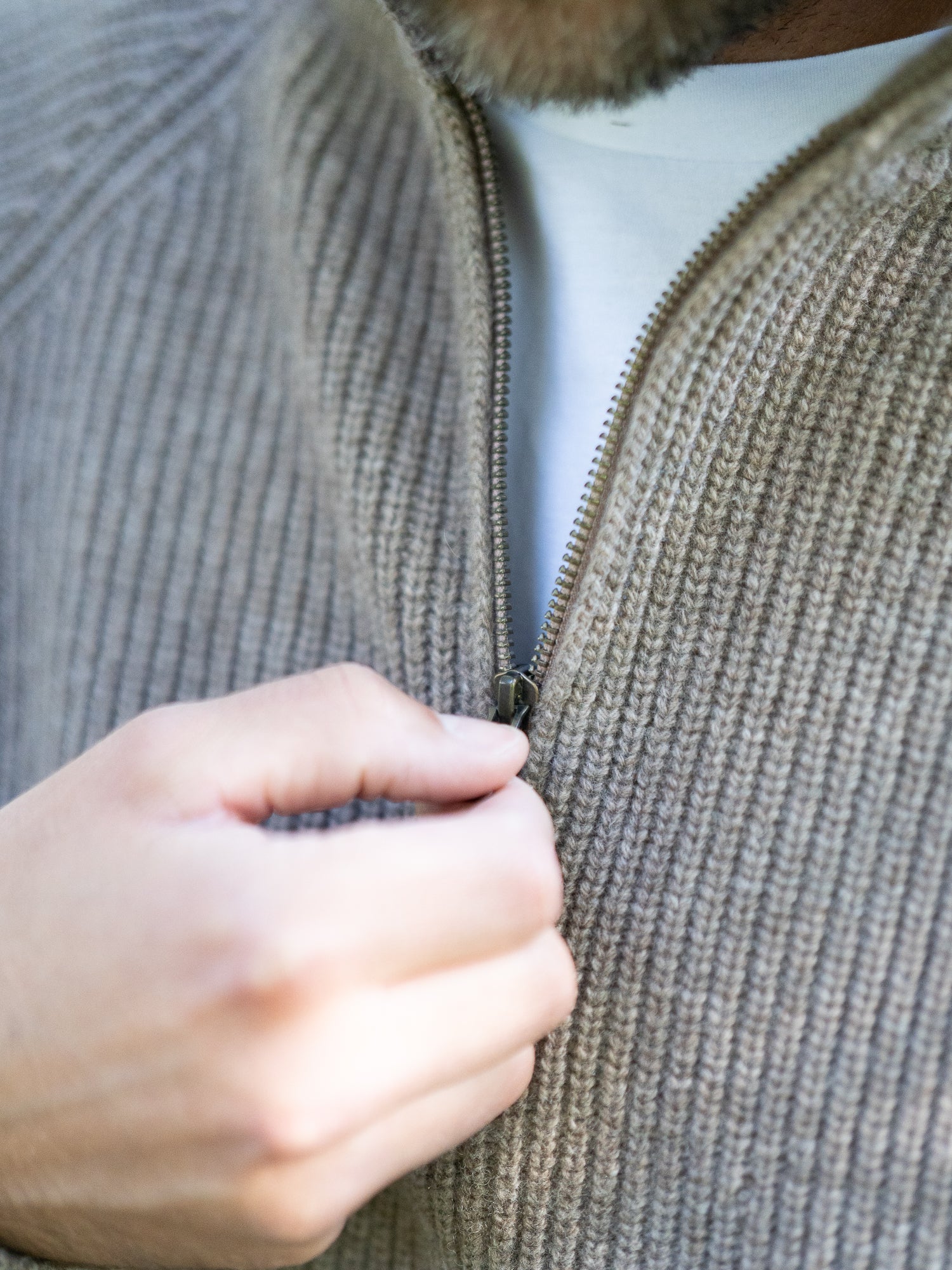 Nachhaltiger Fair Fashion Männer Merino Troyer in braun meliert aus 100% Merino Schurwolle Made in Italy, getragen von einem jungen Mann der die Hand am Reissverschluss hat.