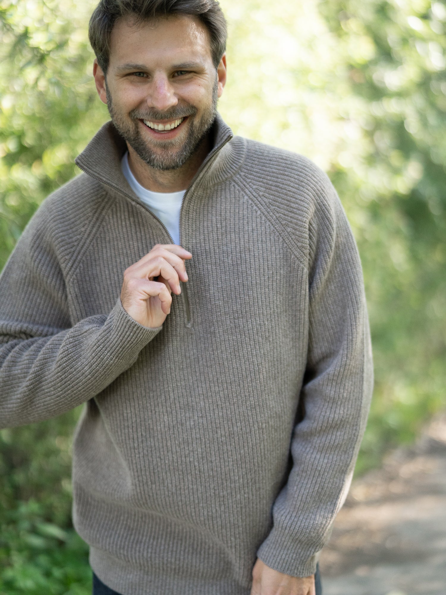 Nachhaltiger Fair Fashion Männer Merino Troyer in braun meliert aus 100% Merino Schurwolle in navy Made in Italy, getragen von einem jungen Mann der in die Kamera lacht.