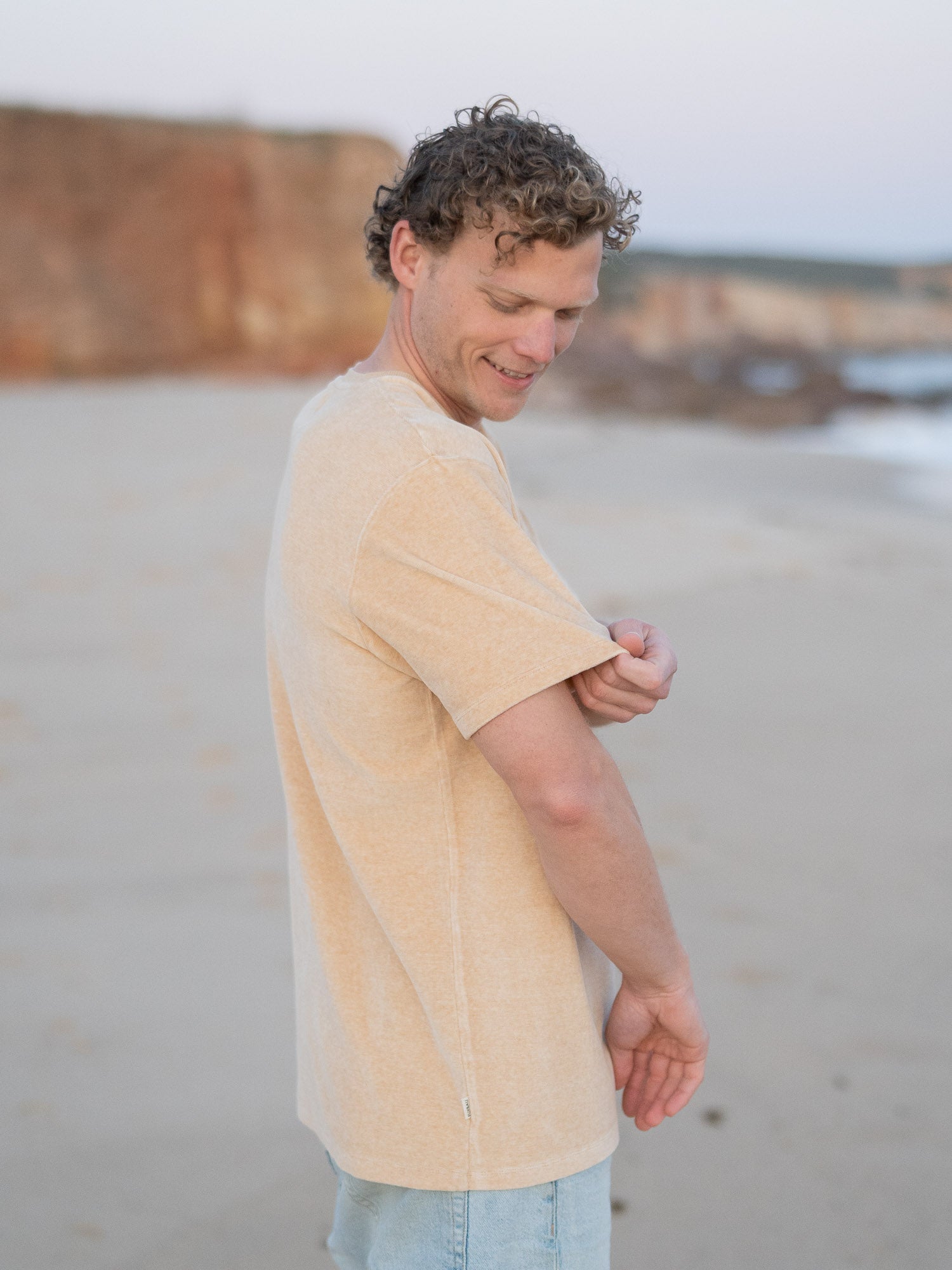 Nachhaltiges Fair Fashion Männer Samt T-Shirt in gelb beige geriffelt aus 100% GOTS zertifizierter Biobaumwolle. Gefertigt in Portugal und getragen am Strand in Portugal.